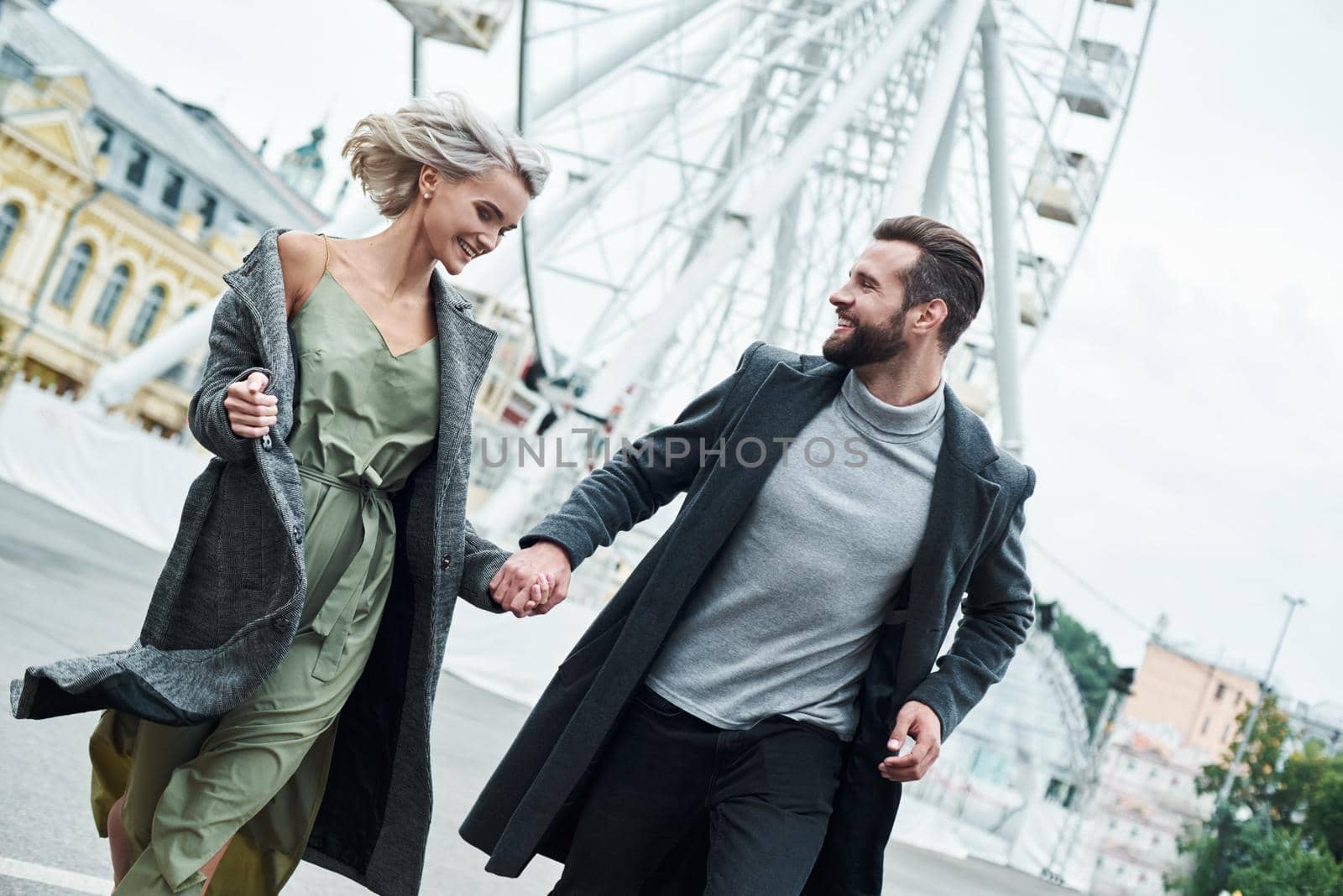 Romantic date outdoors. Young couple running at entertainment park holding hands looking at each other smiling happy