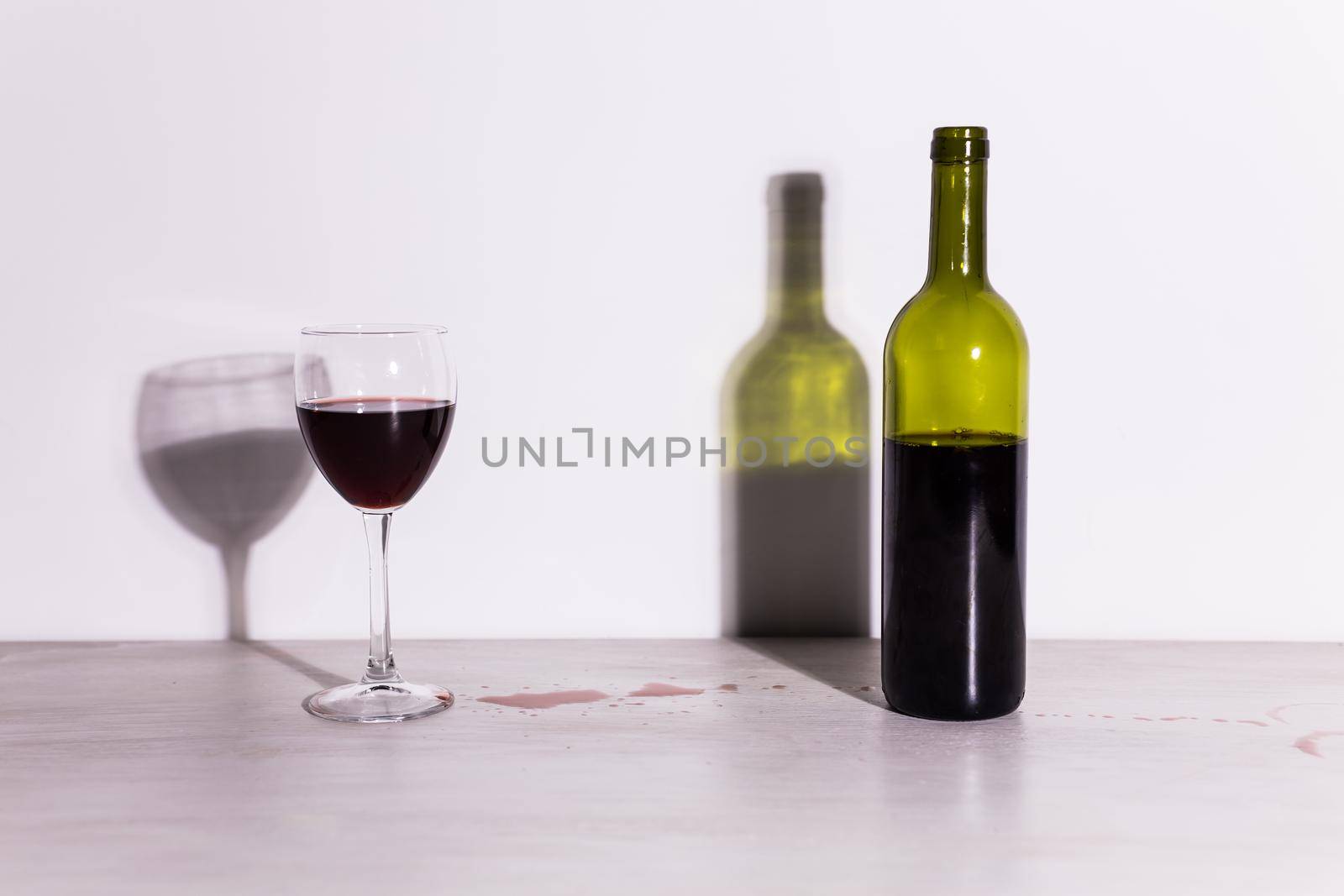 Bottle with wine and glass, red puddle of wine on the table. Cleaning after party concept