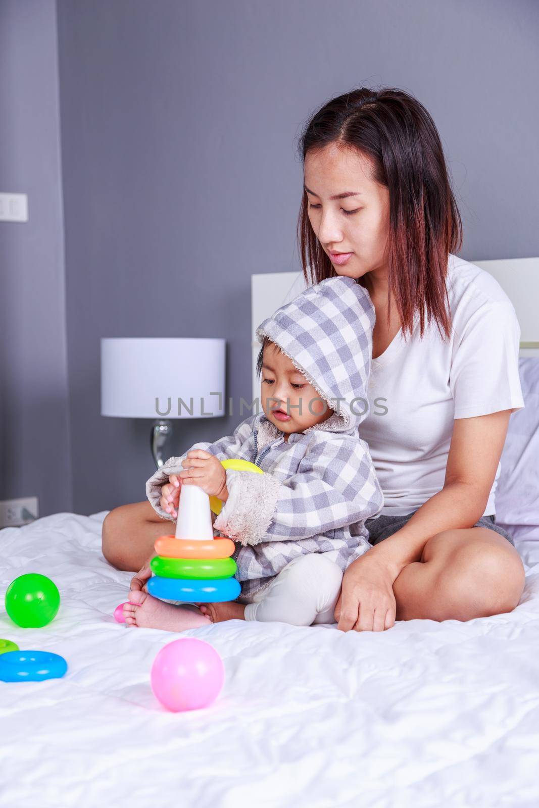 baby playing toys with mother on bed at home