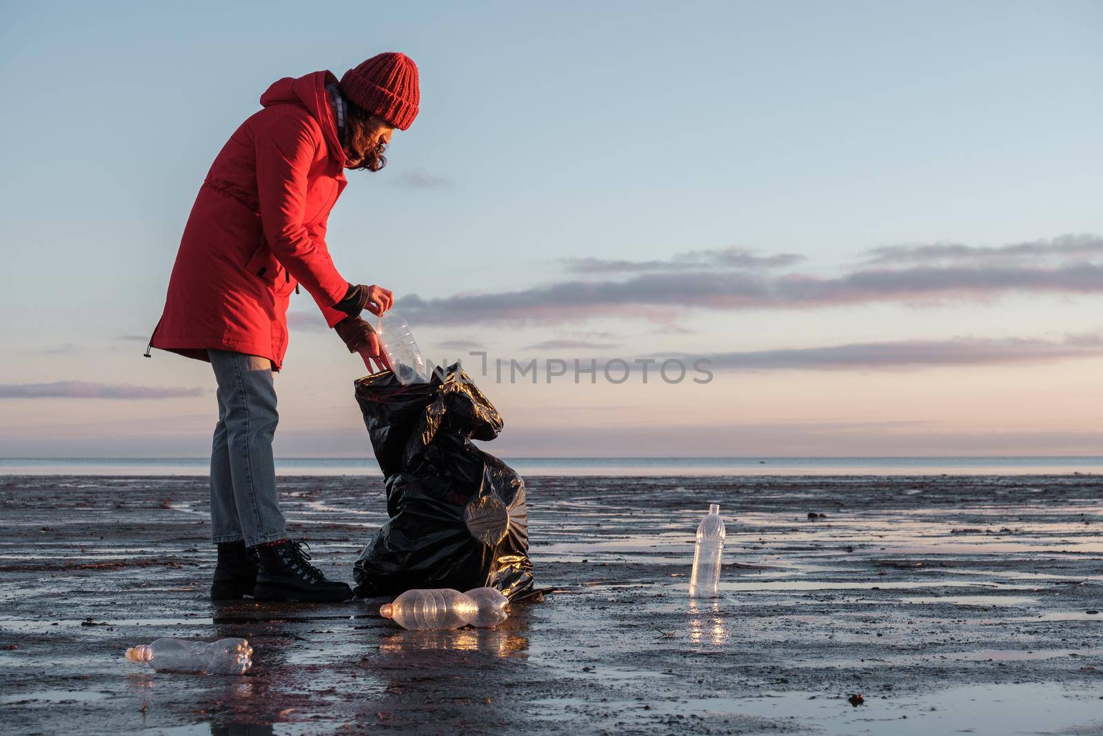 A woman cleans the bank of plastic bottles and puts the trash in a garbage bag by vollirikan
