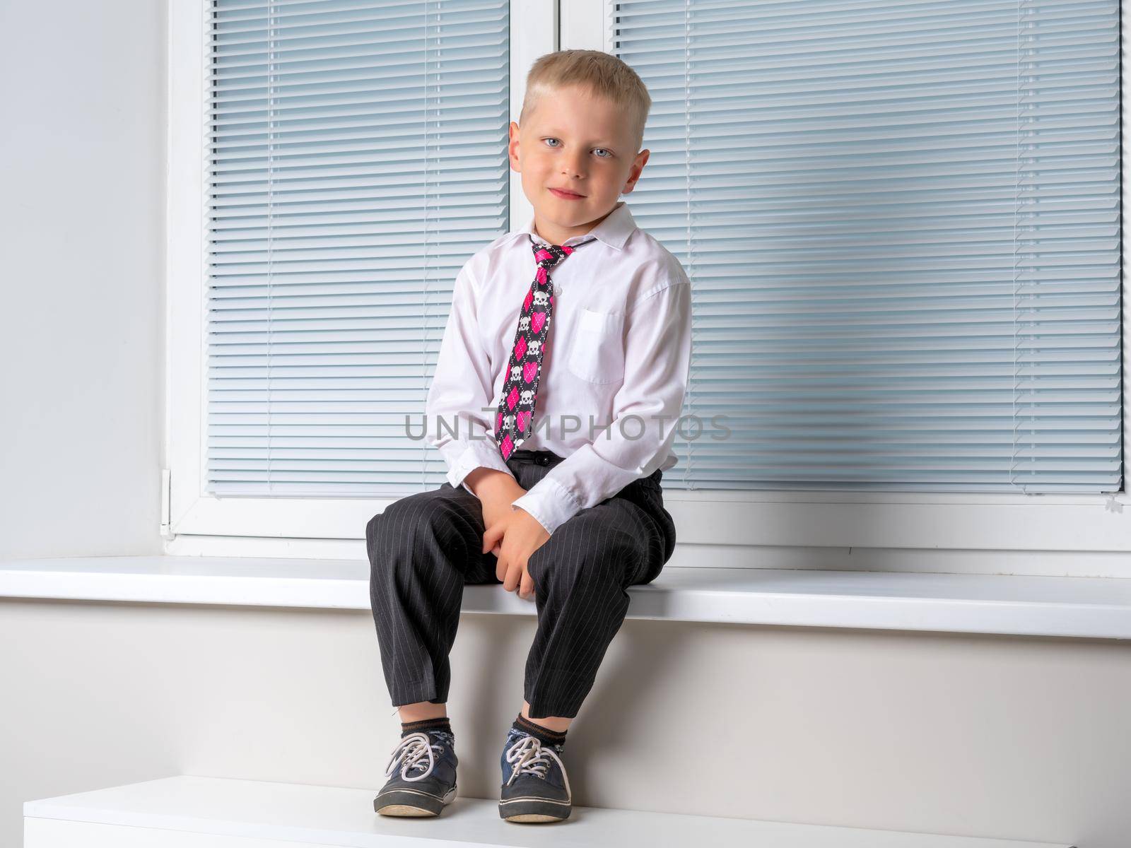 A little boy is sitting near the window on the windowsill. by kolesnikov_studio