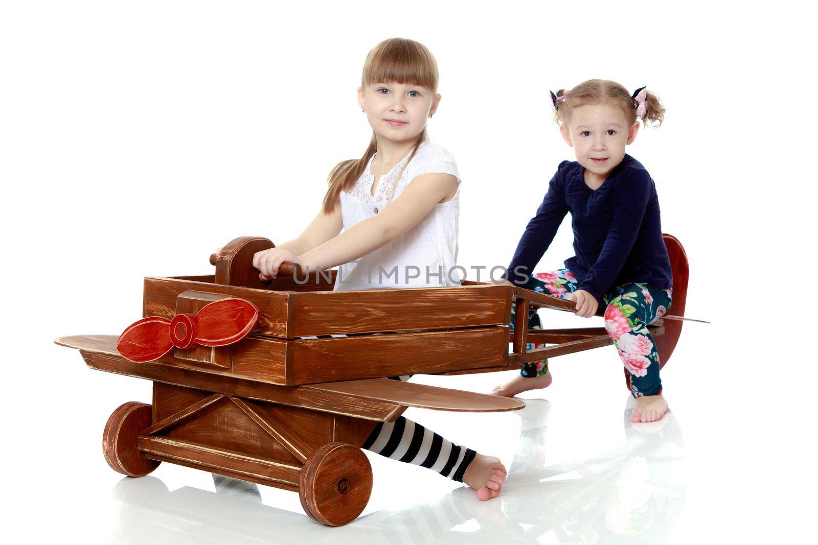 Two girls sister play with a wooden plane. The concept of a happy childhood, playing in the family. Isolated on white background.