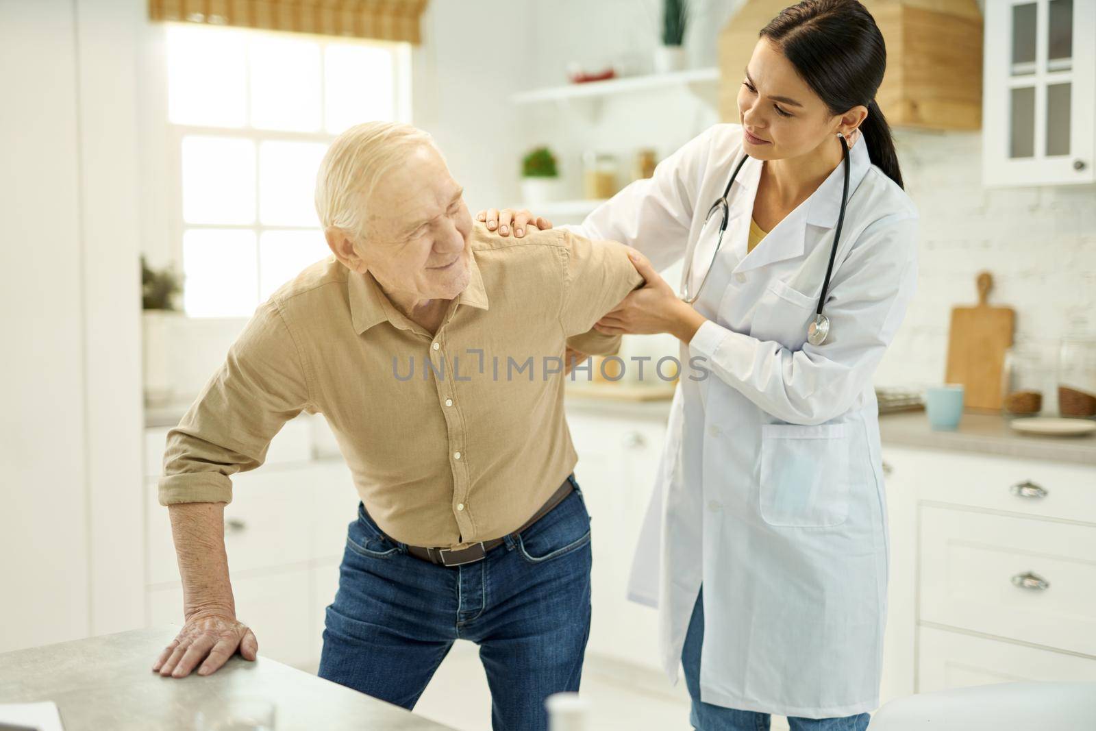 Helpful female doctor assisting senior patient with getting up from the chair