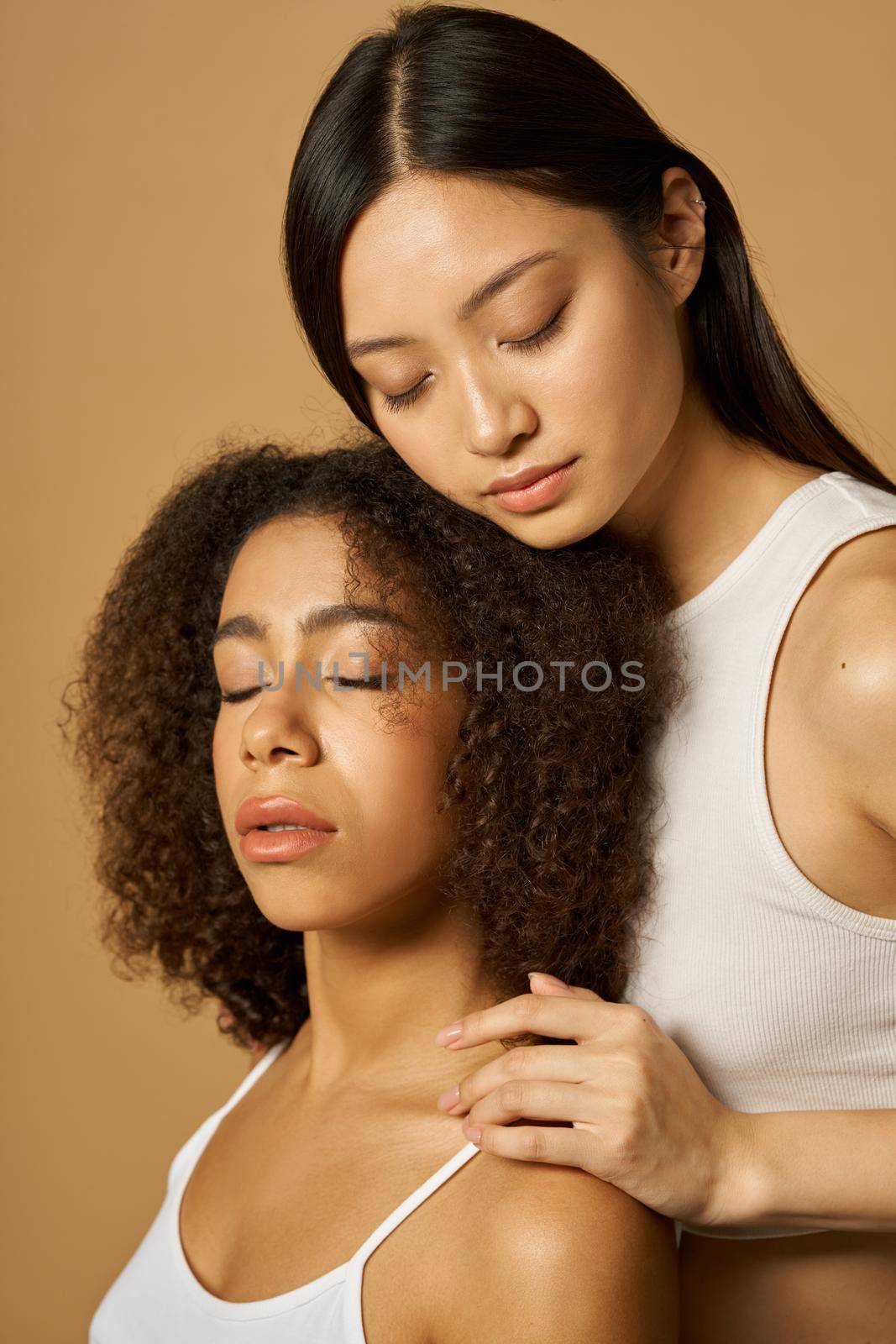 Beauty portrait of two gorgeous mixed race young women with perfect glowing skin posing together isolated over light brown background. Skincare, diversity concept