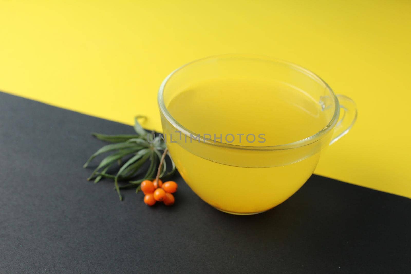 sea buckthorn tea drink on a black yellow bright background. Sea buckthorn drink tea juice in a glass cup next to a spout of sea buckthorn leaves orange berries on a black and yellow background. Creative creative photography. Seasonal berry.