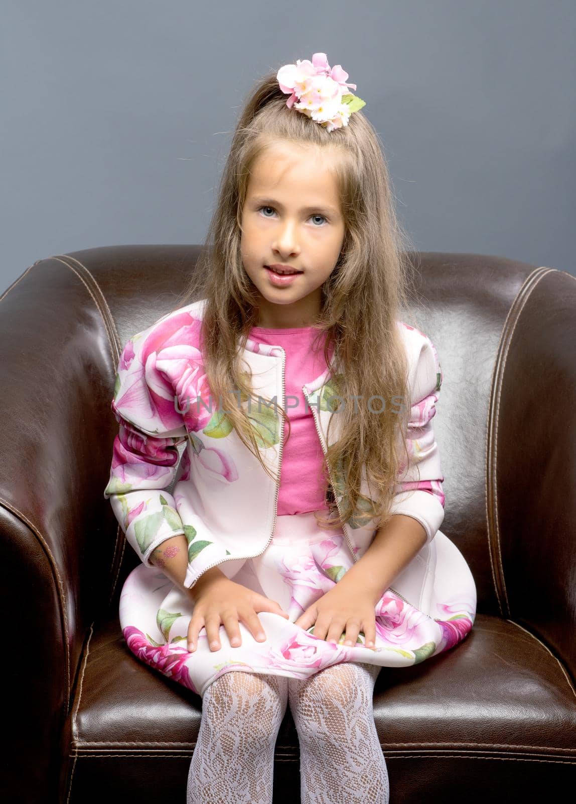 A little girl is sitting on a leather chair. by kolesnikov_studio