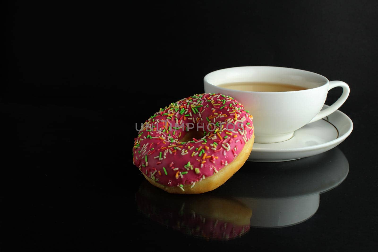 Doughnut with pink icing berliner lies next to a cup of coffee tea delicious breakfast snack day without diet on black background copyspace.