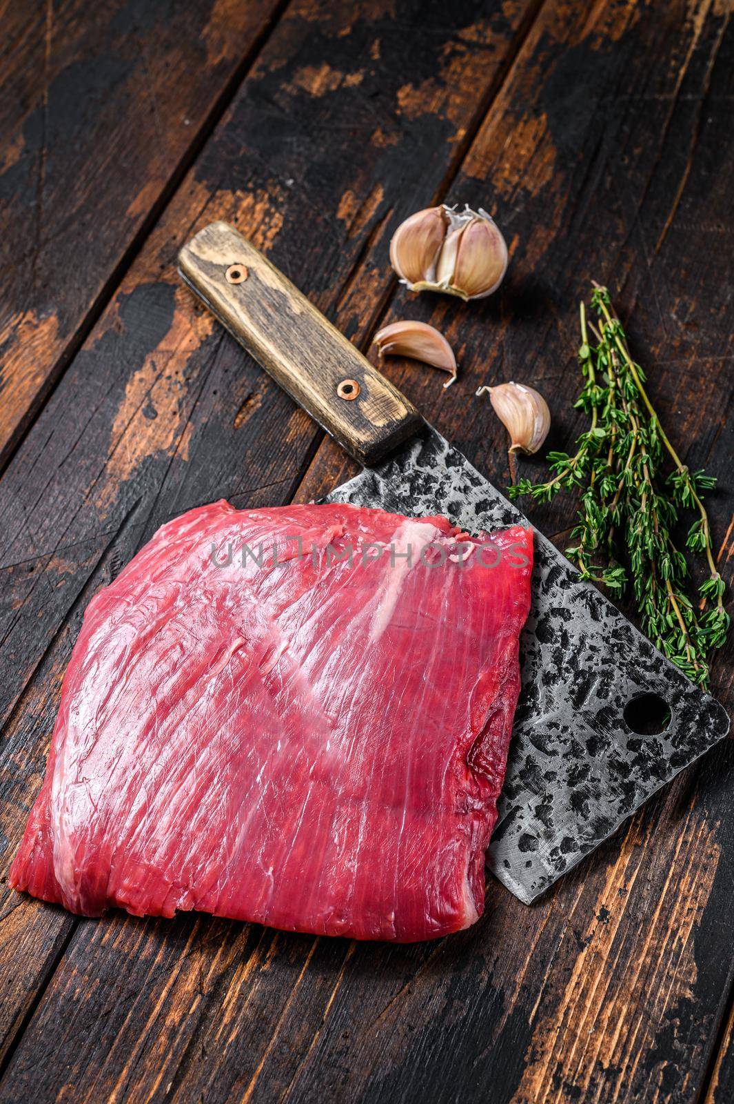 Raw flank beef marbled meat steak on a cleaver. Dark Wooden background. Top view.