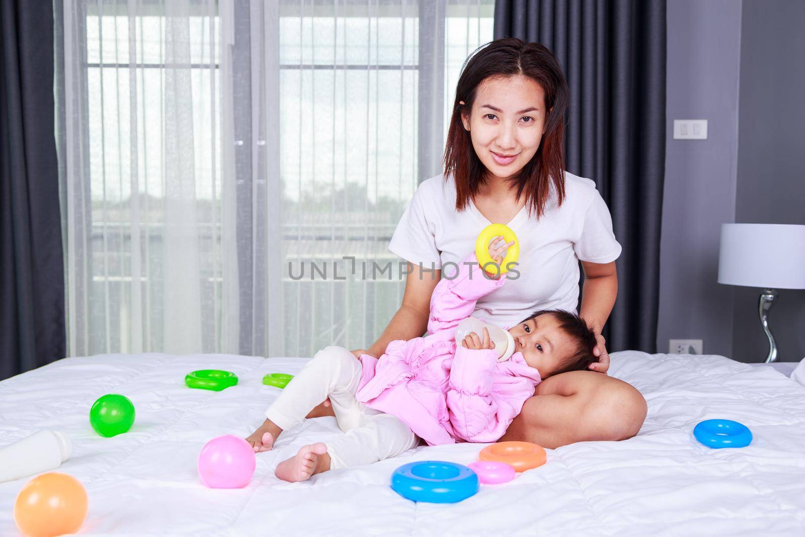 baby drinking a milk from bottle with mother on a bed