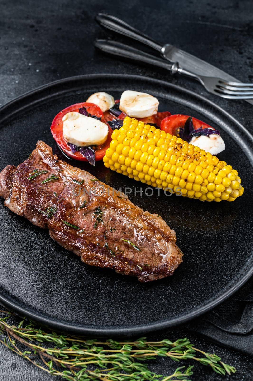 Roasted P beef steaks Striploin or New York on a plate with garnish. Black background. Top view.