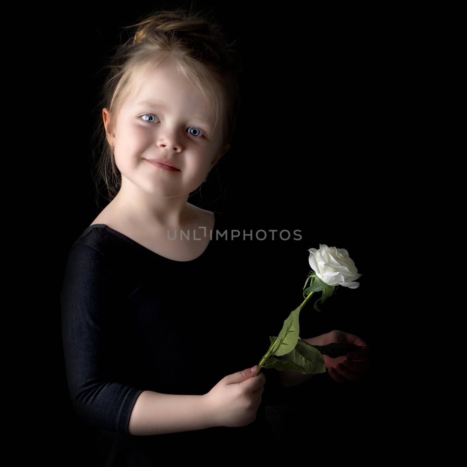 Beautiful little girl with a flower in her hand. The concept of style and fashion. On a black background.