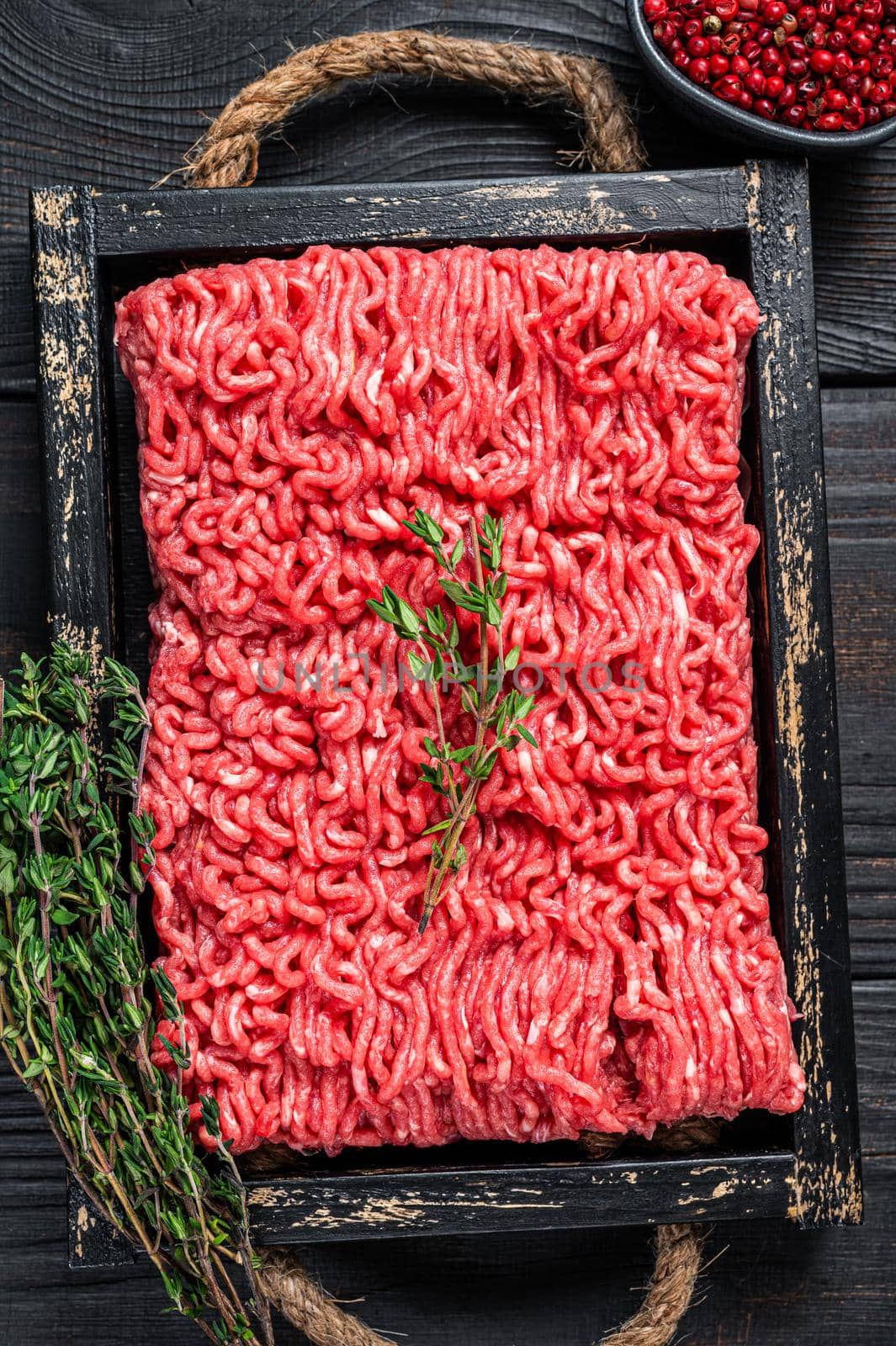 Raw mince ground beef and pork meat in a wooden tray with herbs. Black background. Top view.