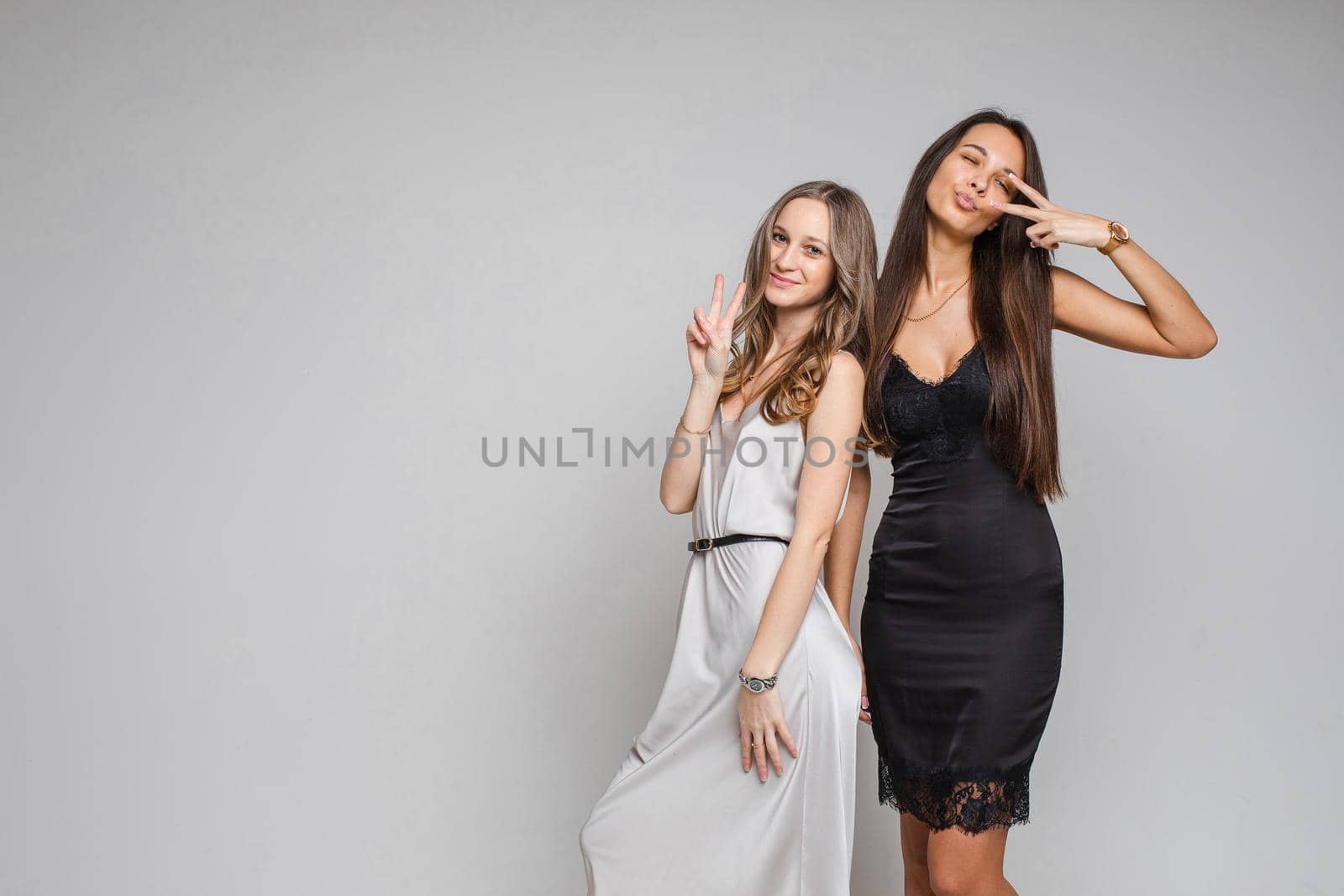 two girlfriends with brown hair in beautiful black and white dresses celebrate new year with smile by StudioLucky