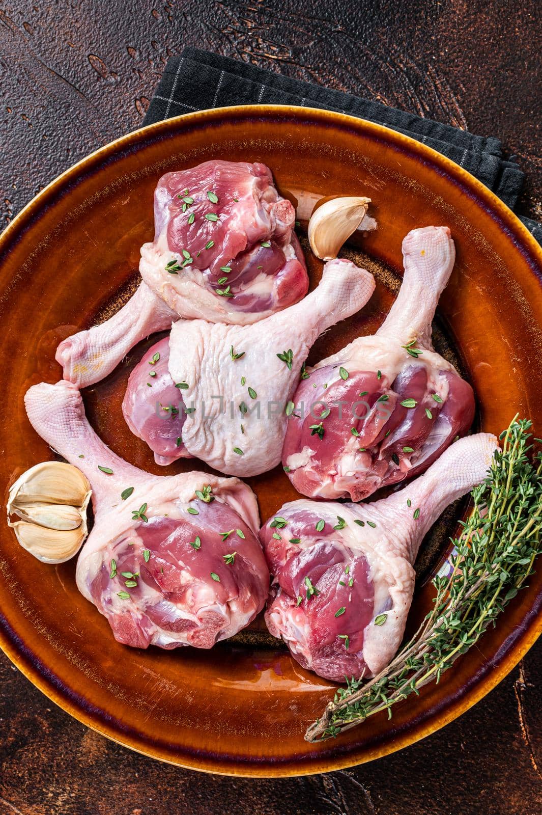Raw Poultry meat - Duck legs drumsticks on a rustic plate with herbs. Dark background. Top view.