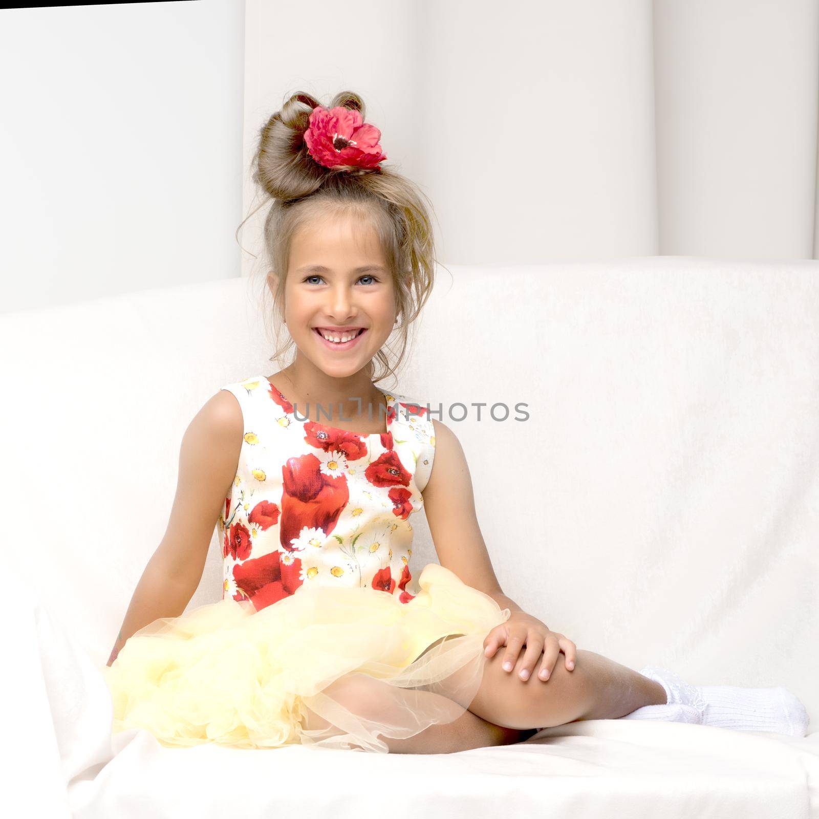 A little girl is sitting on the couch in a photo studio. Isolated on white background