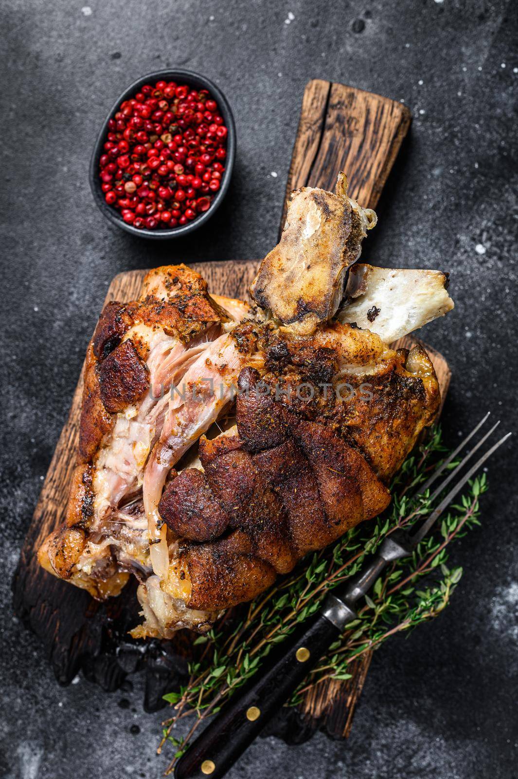 Roasted pork knuckle eisbein on a wooden board with herbs. Black background. Top view.