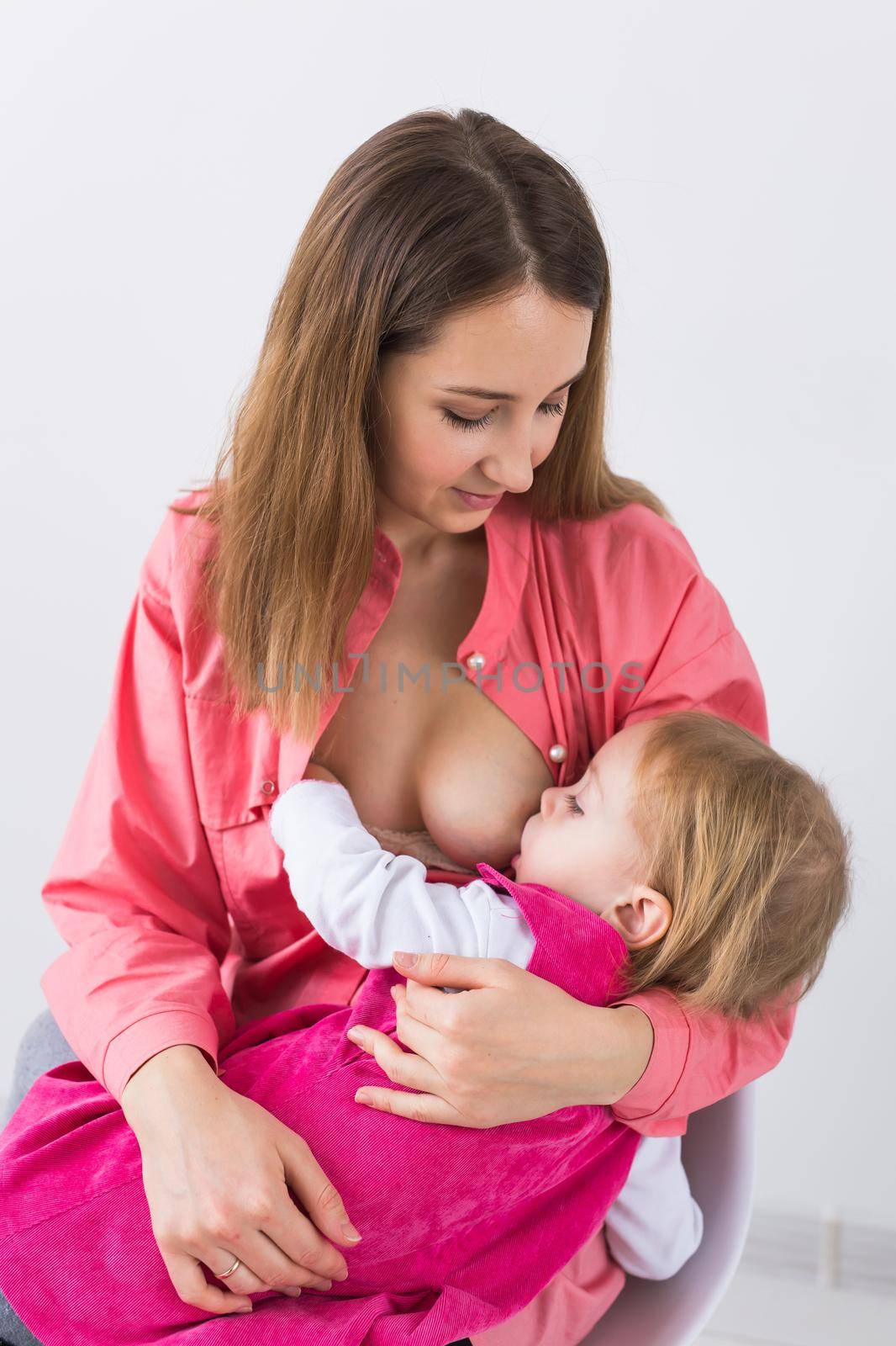 Mother breastfeeding baby in her arms at home. Child eating mother's milk. Young woman nursing and feeding baby. Concept of lactation infant. by Satura86