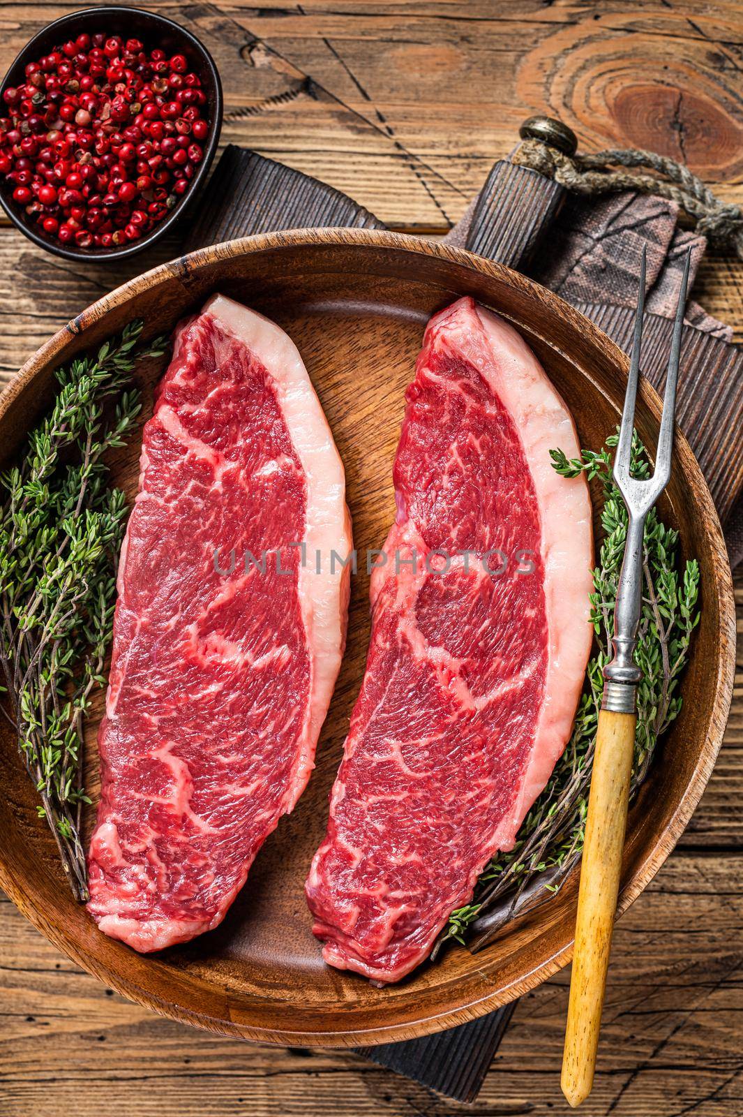 Uncooked Raw top sirloin cap beef meat steaks in a wooden plate with herbs. woden background. Top view.