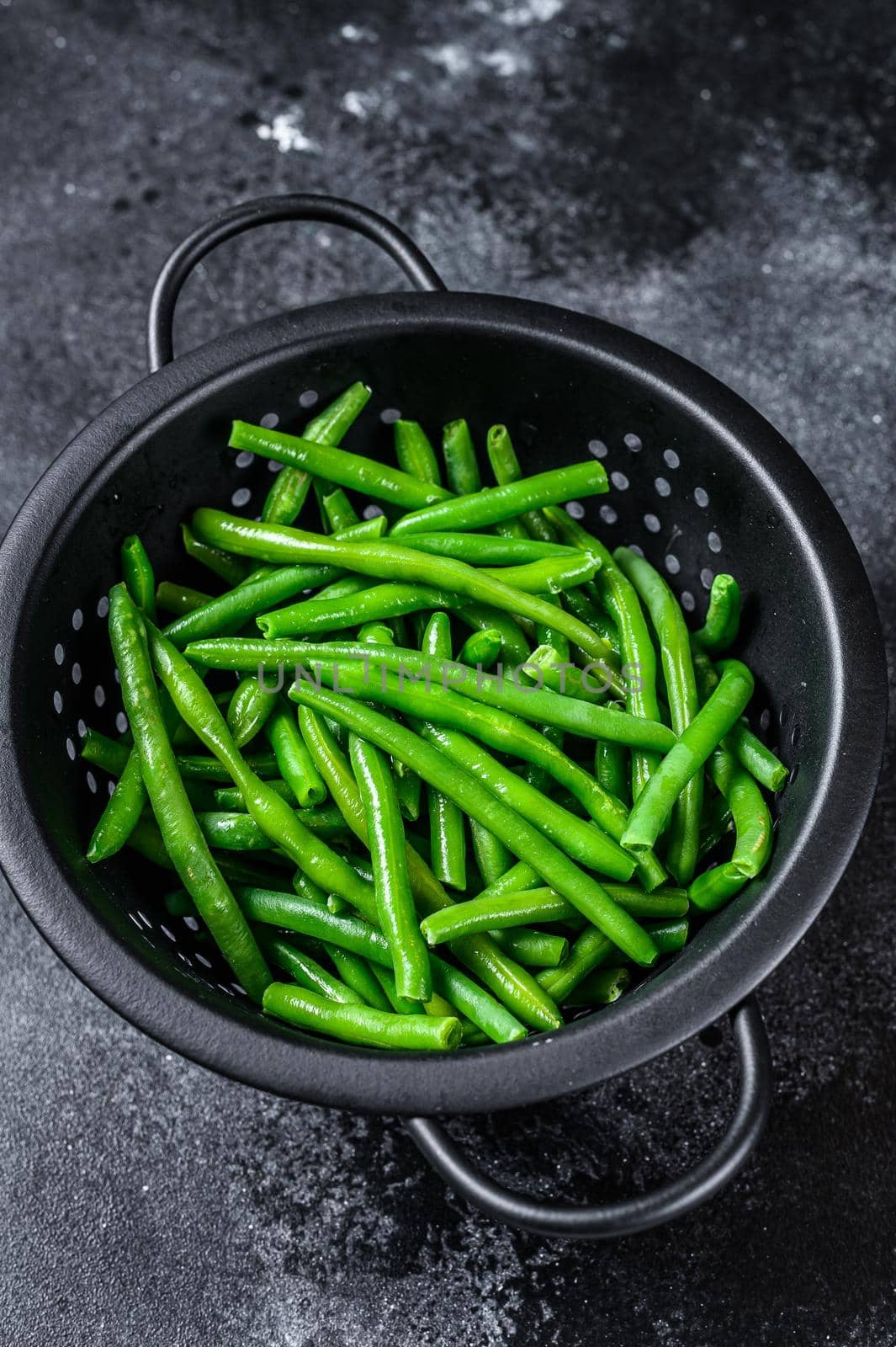 Raw green beans in a colander. Black background. top view.