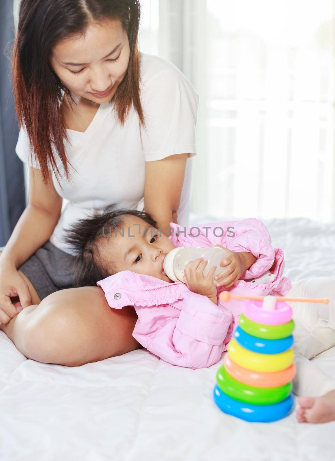 baby drinking a milk from bottle with mother on a bed