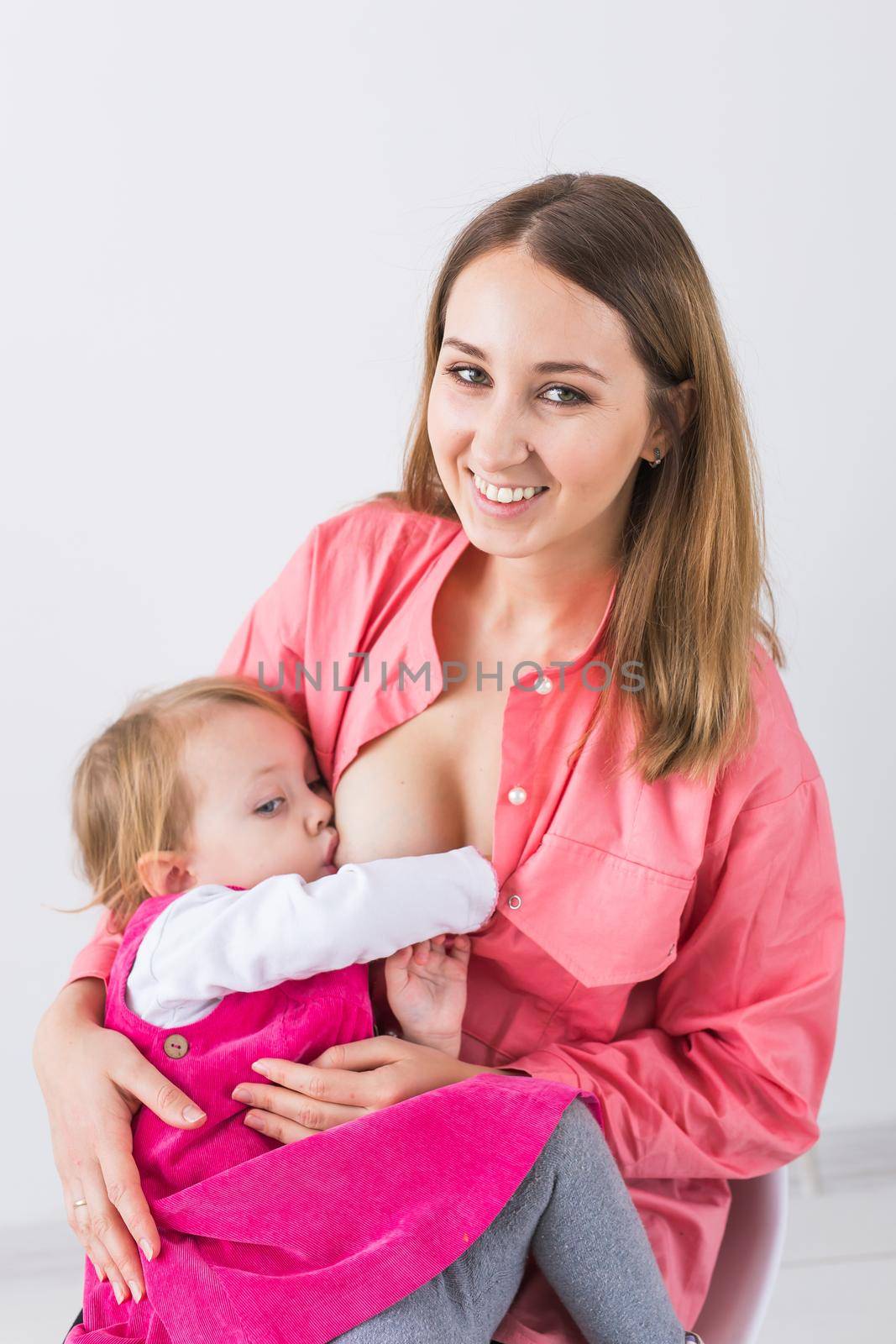 Lactation and motherhood concept - Young beautiful mother holding breastfeeding baby sitting on chair. by Satura86