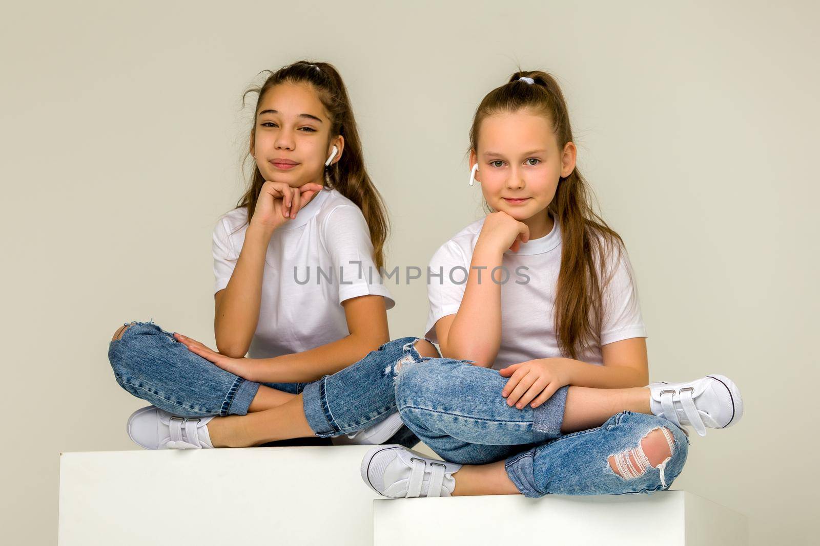 Two little girls posing in the studio on white cubes. The concept of tenderness and beauty.