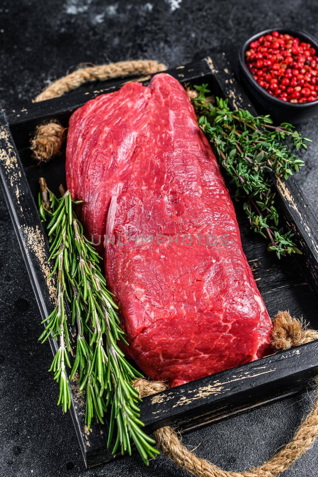 Raw Whole Tenderloin veal meat on a wooden tray with herbs. Black background. Top view.