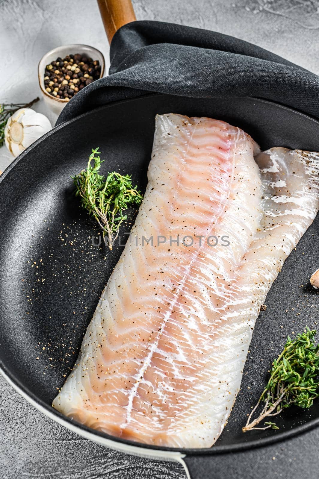 Raw cod loin with herbs in a frying pan. Gray background. Top view.