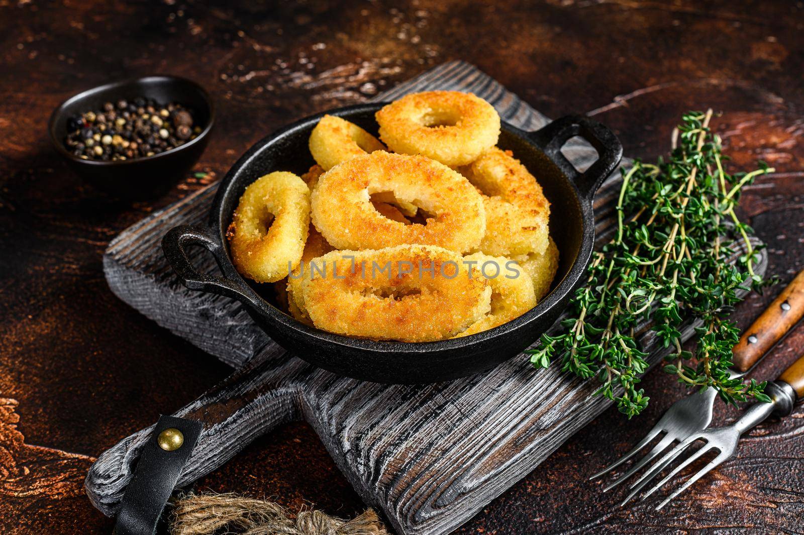 Fried squid rings breaded on a cutting board. Dark background. Top view.