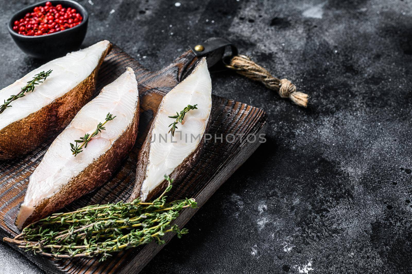 Raw fresh halibut fish steak on a wooden cutiing board. Black background. Top view. Copy space.