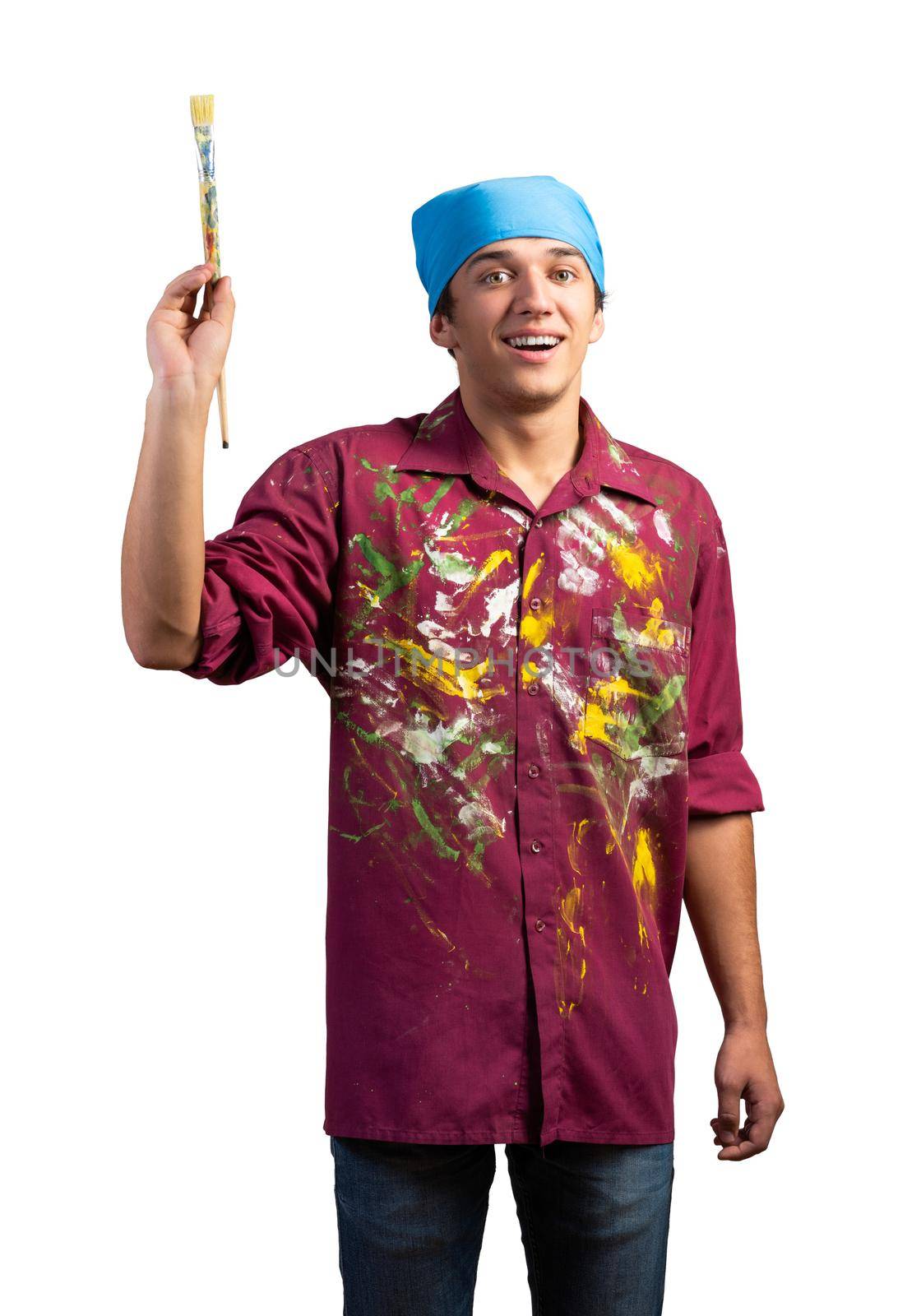 Smiling young painter artist pointing upwards with paintbrush in hand. Portrait of happy painter isolated on white background. Creative hobby and artistic occupation. Art school student posing.