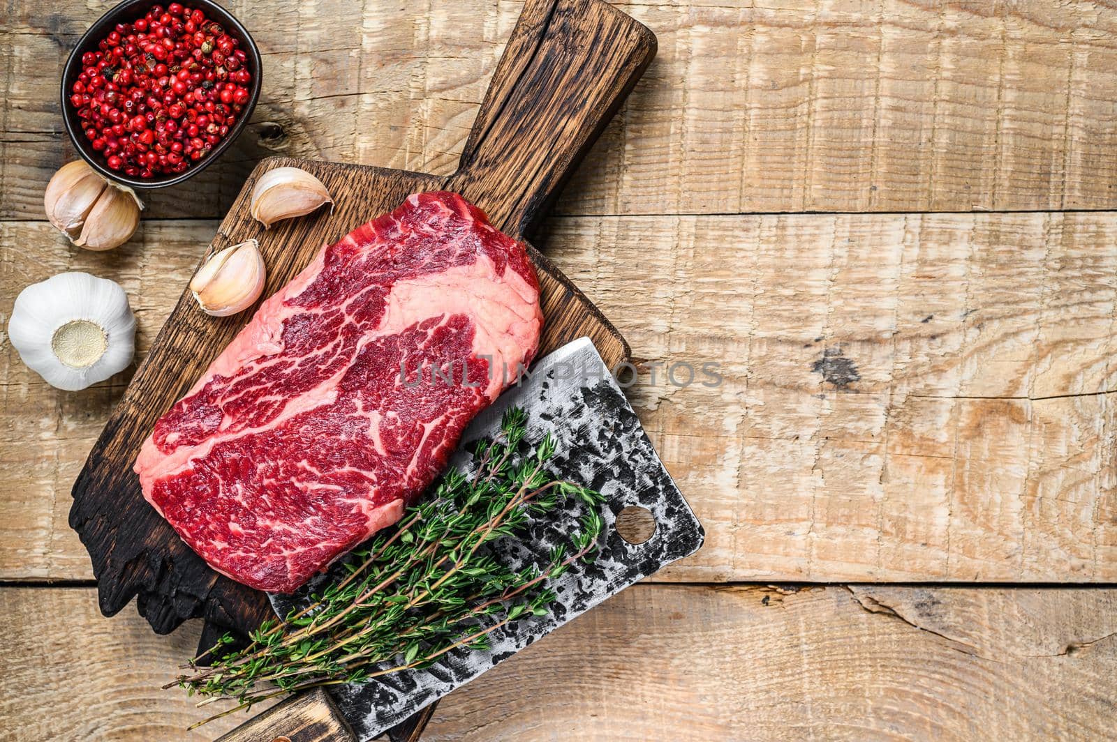 Prime rib eye raw beef meat steak on a butcher wooden cutting board with cleaver. wooden background. Top view. Copy space.