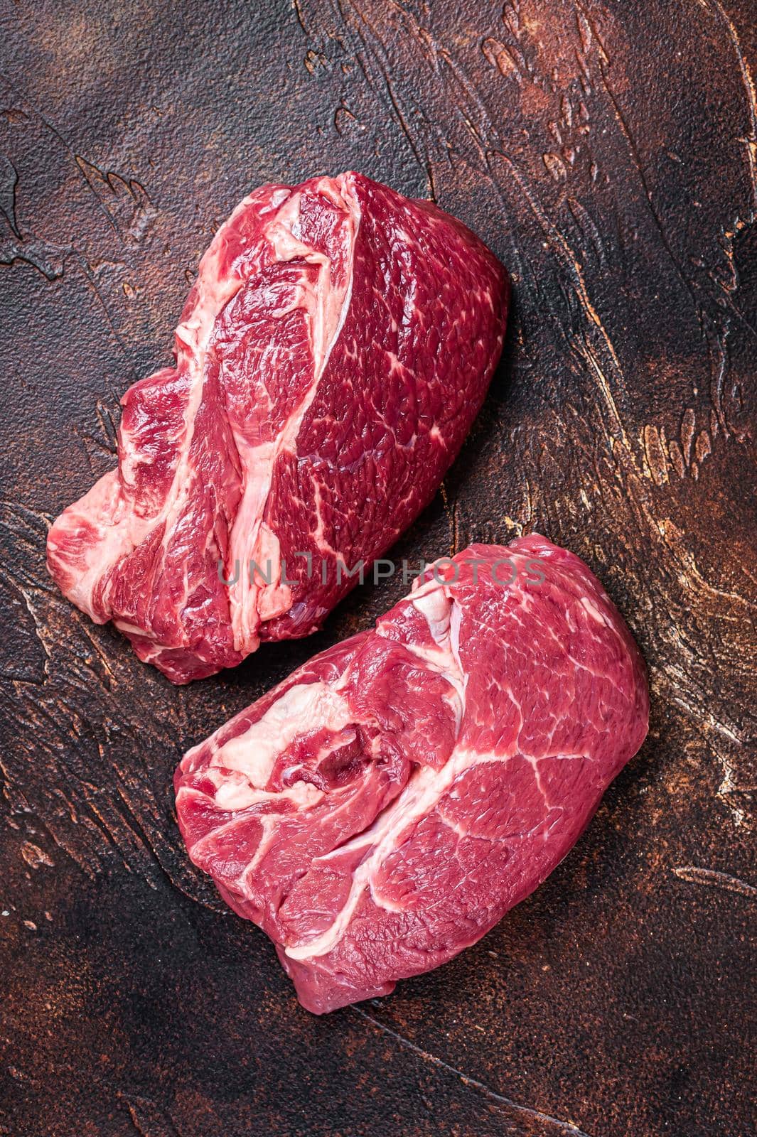 Raw Chuck eye roll beef steak on butcher table. Dark background. Top view.