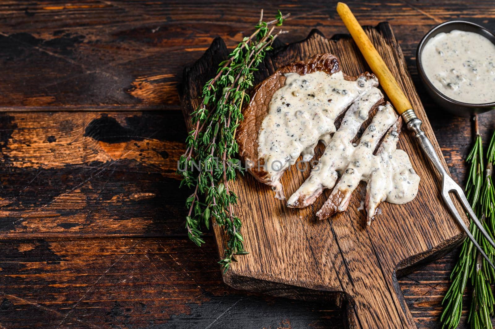 Roast fillet beef meat steak with peppercorn sauce on wooden board. Dark wooden background. Top view. Copy space.