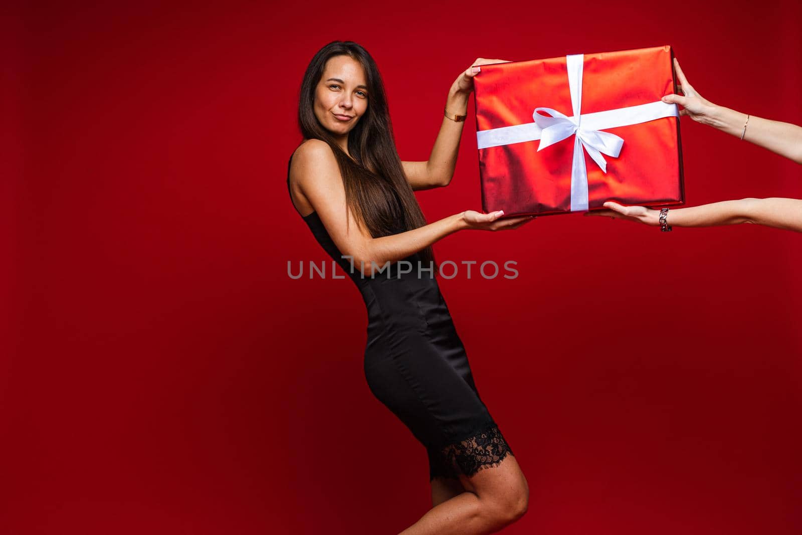 Portrait of laughing brunette in black dress with lace rim getting giant present in red paper and white bow on Valentine s day.