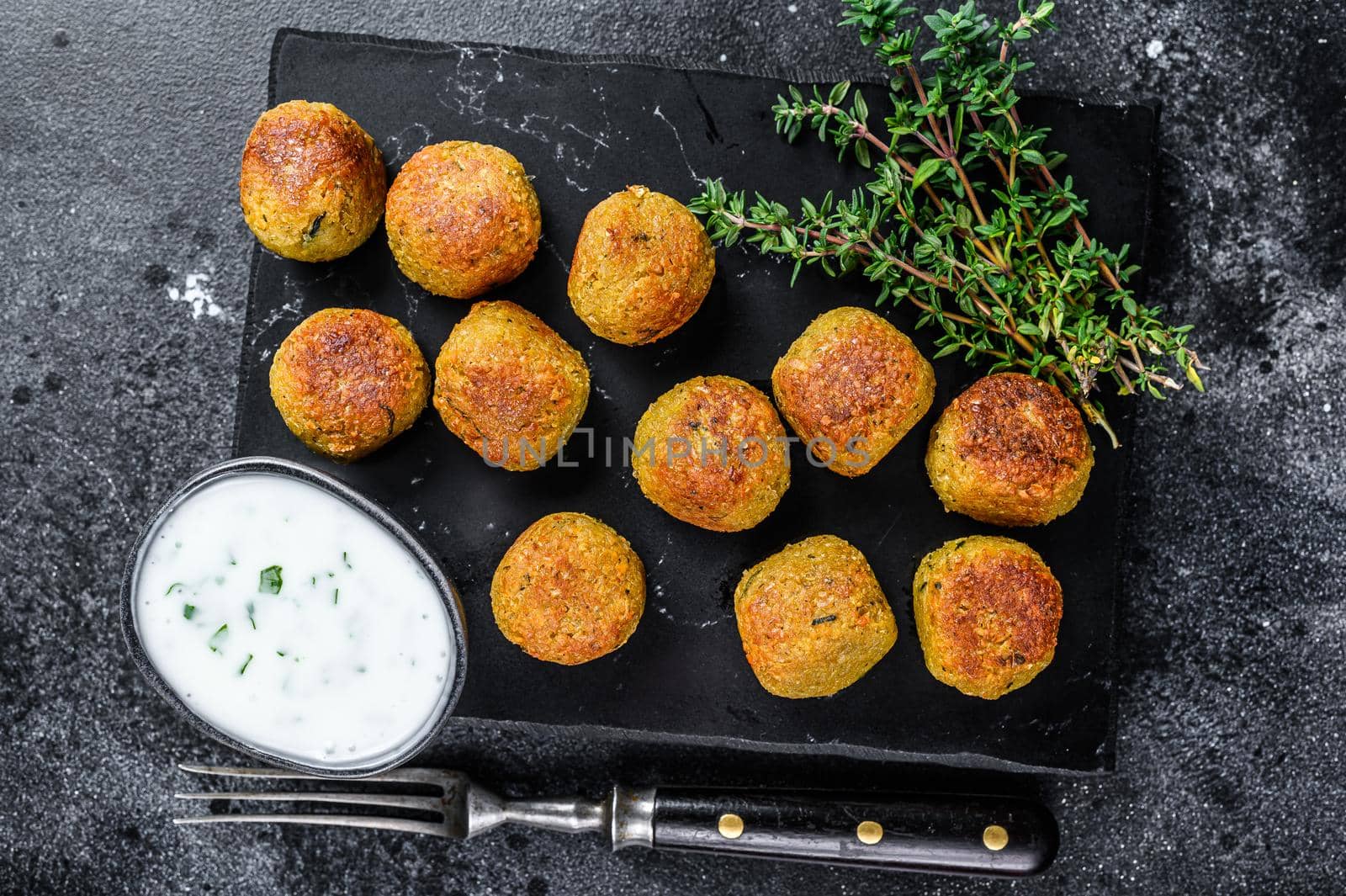 Roasted vegetarian falafel balls from spiced chickpeas with garlic yogurt sauce. Black background. Top view.