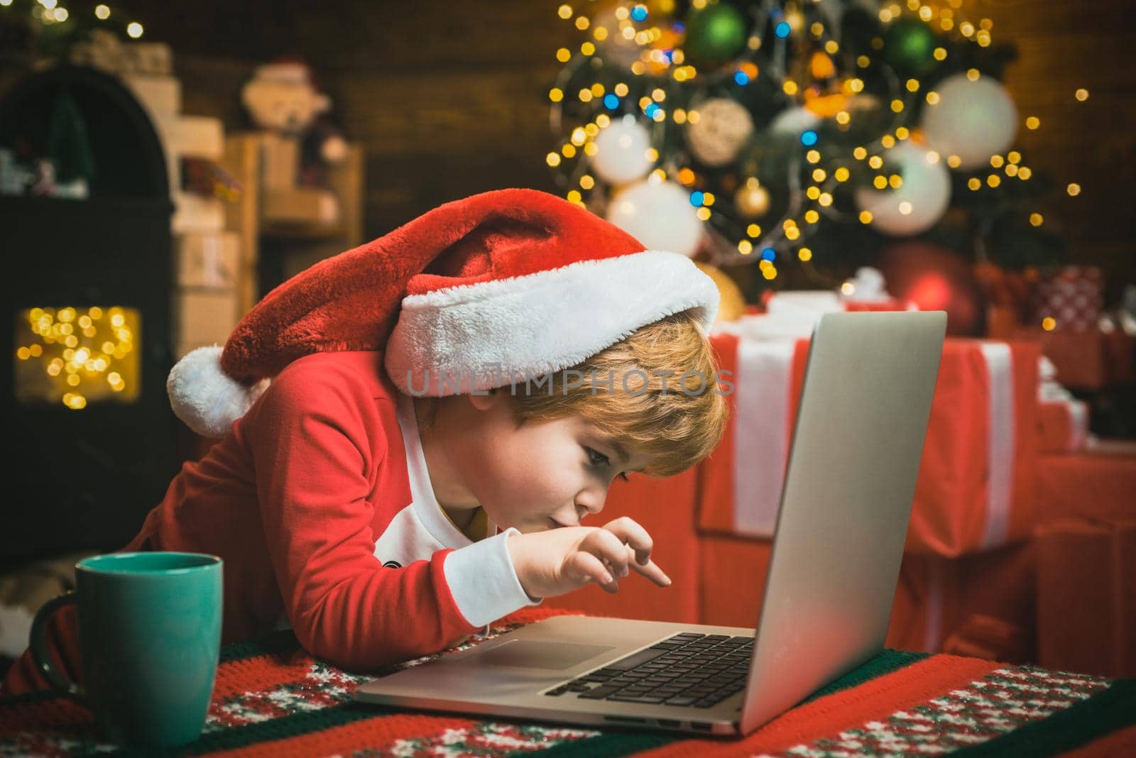 Christmas child boy typing letter to Santa Claus on a laptop at home on Christmas background. by Tverdokhlib