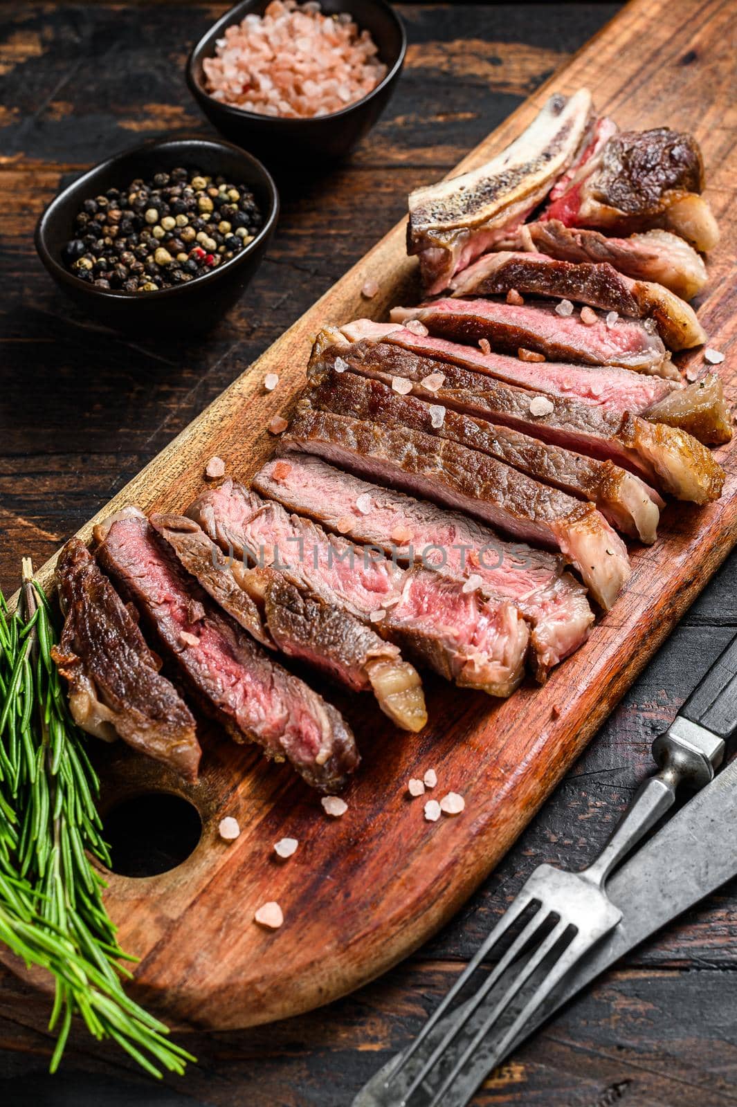 Grilled cowboy or rib eye beef steak with herbs and spices. Wooden dark background. Top view
