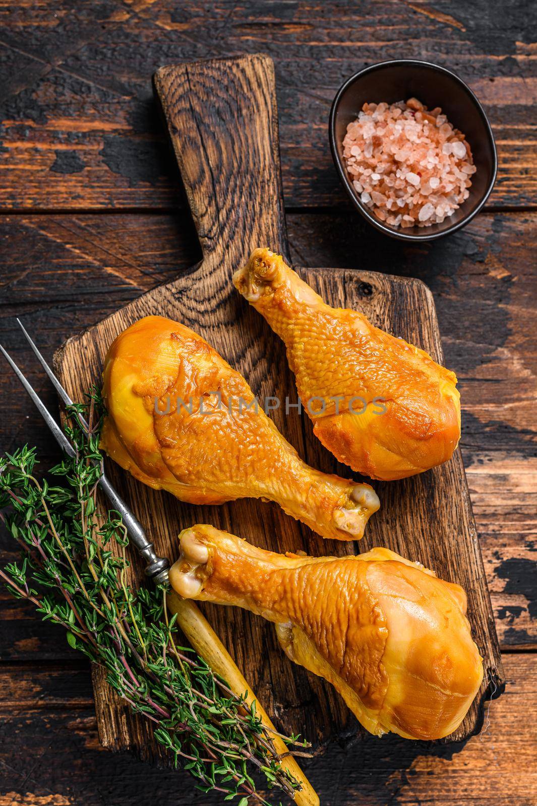 Marinated and Smoked chicken legs drumsticks on a wooden cutting board. Dark wooden background. Top view by Composter