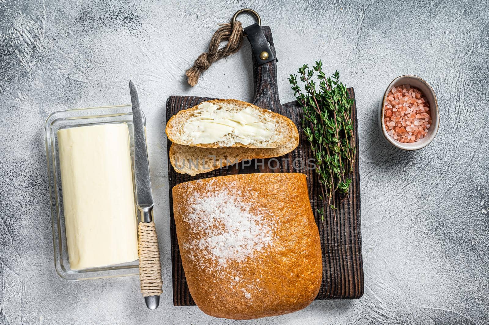 Butter block and sliced toasts of bread on a wooden board with herbs. White background. Top view by Composter