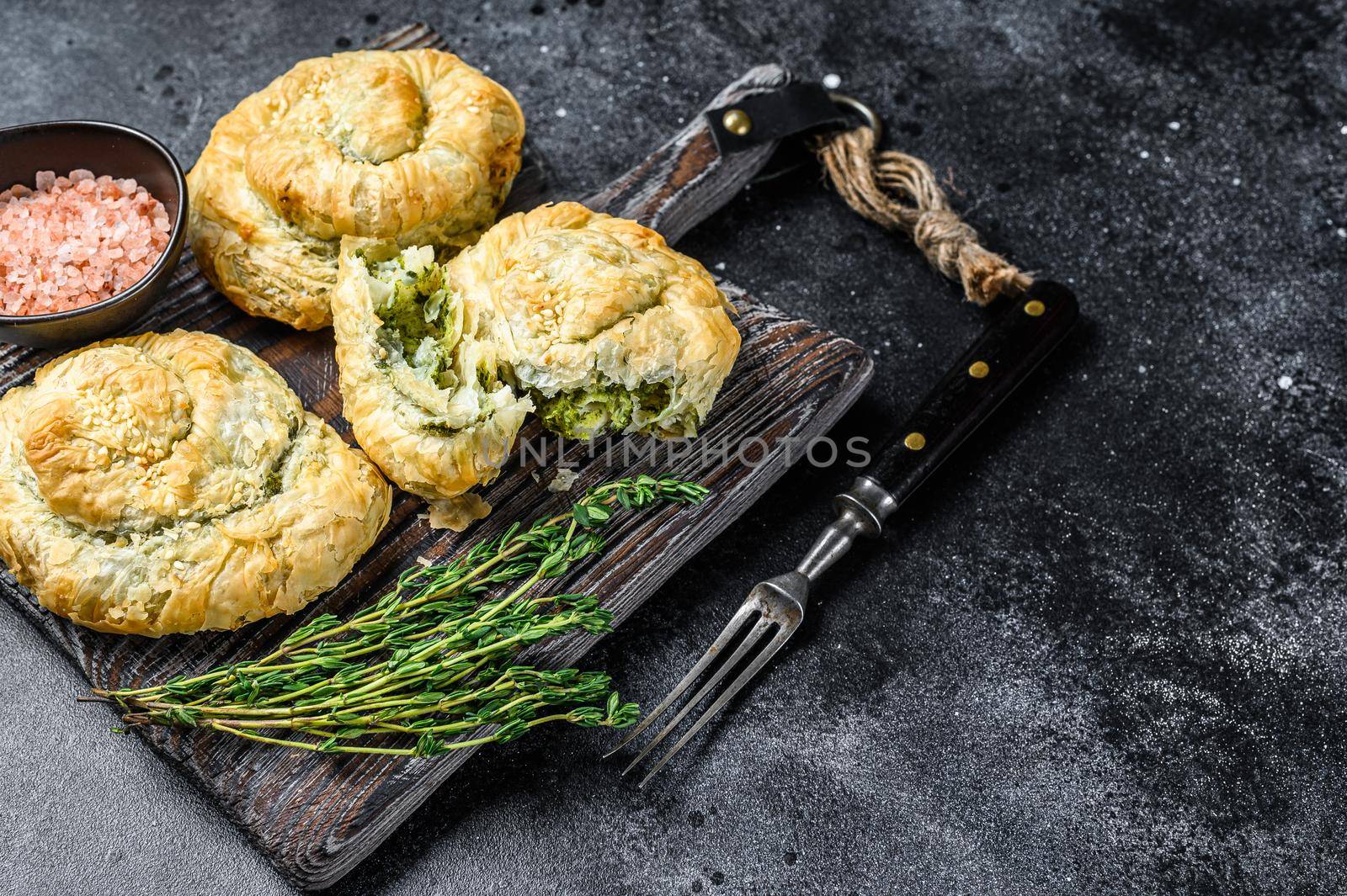 Baked Spanakopita spiral filo pastry puff pie with feta cheese and spinach. Black background. Top view. Copy space by Composter