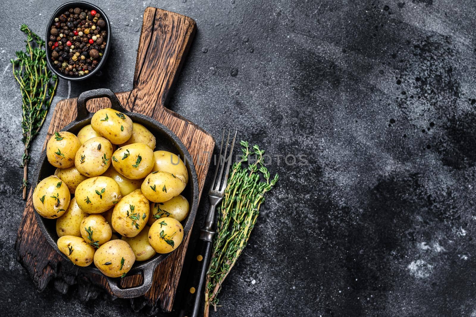 Young baby boiled potato with butter in a pan. Black background. Top view. Copy space.