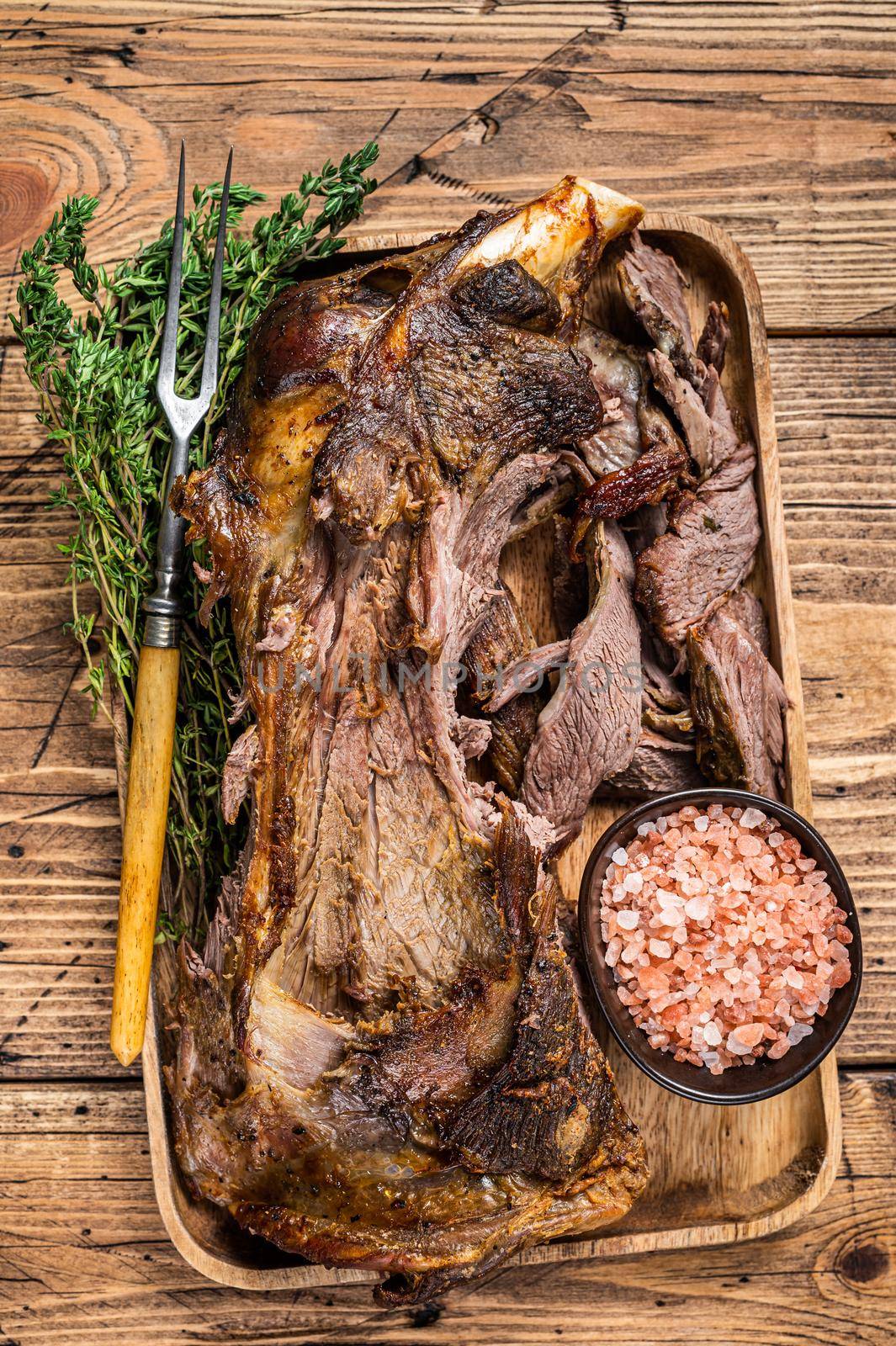 Roasted lamb mutton cutting shoulder meat in a wooden tray with meat fork. wooden background. Top view.