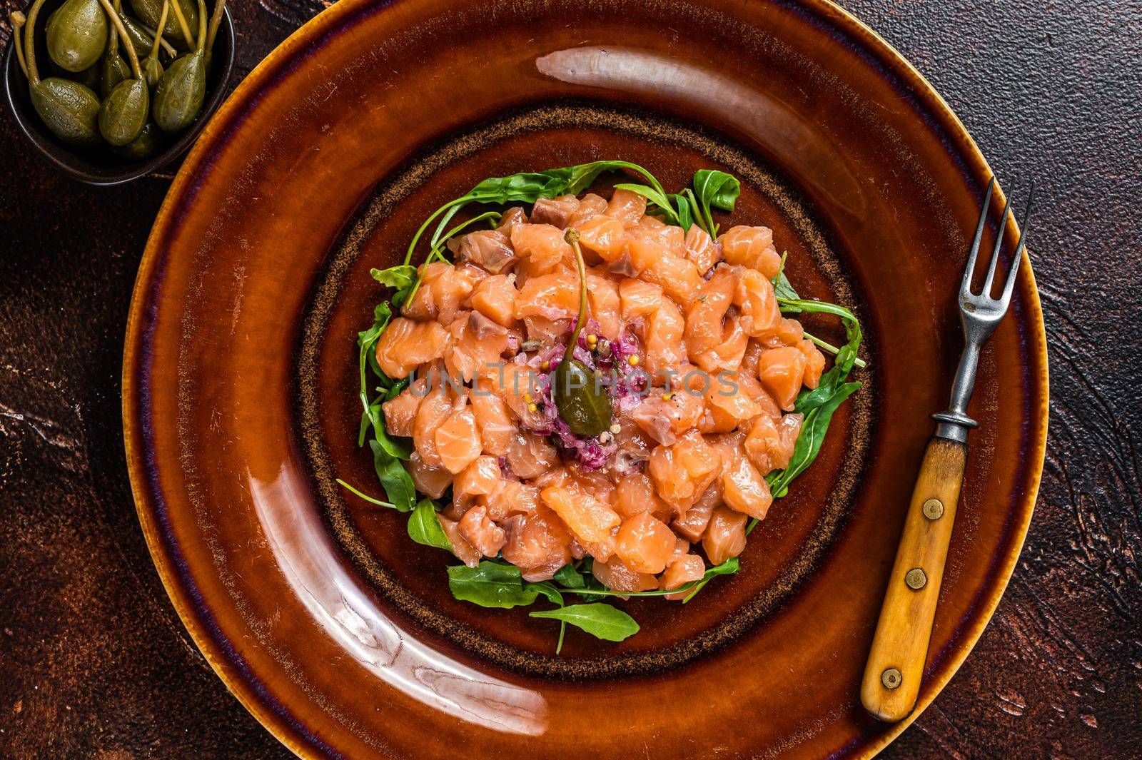 Tartar or tartare with salmon fish, red onion, arugula and capers in rustic plate. Dark background. Top View.