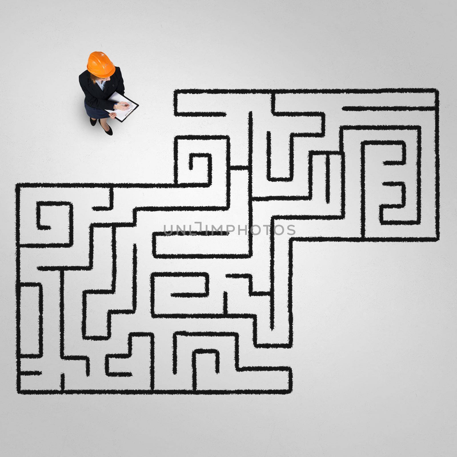 Top view of puzzled businesswoman in helmet looking at drawn maze on floor