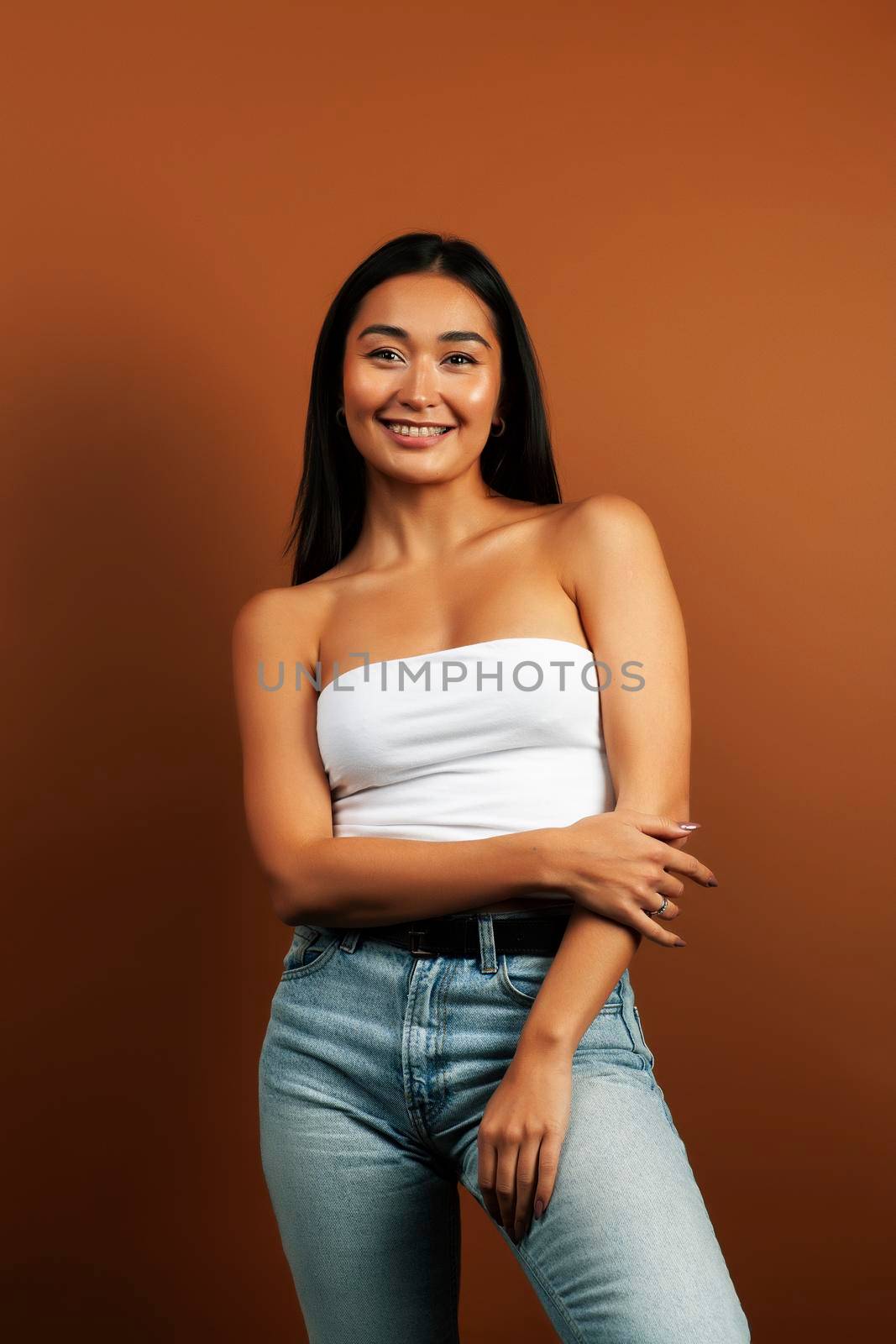 young pretty asian woman cheerful smiling posing on warm brown background, lifestyle people concept close up