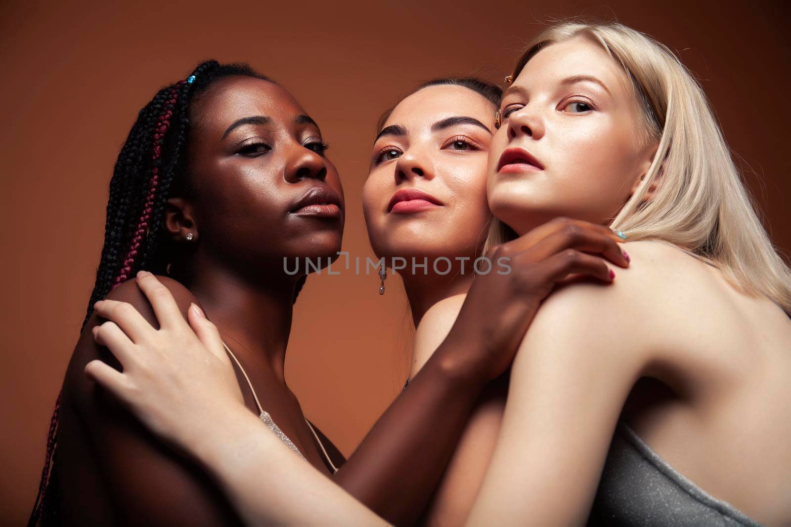 young pretty asian, caucasian, afro woman posing cheerful together on brown background, lifestyle diverse nationality people concept close up