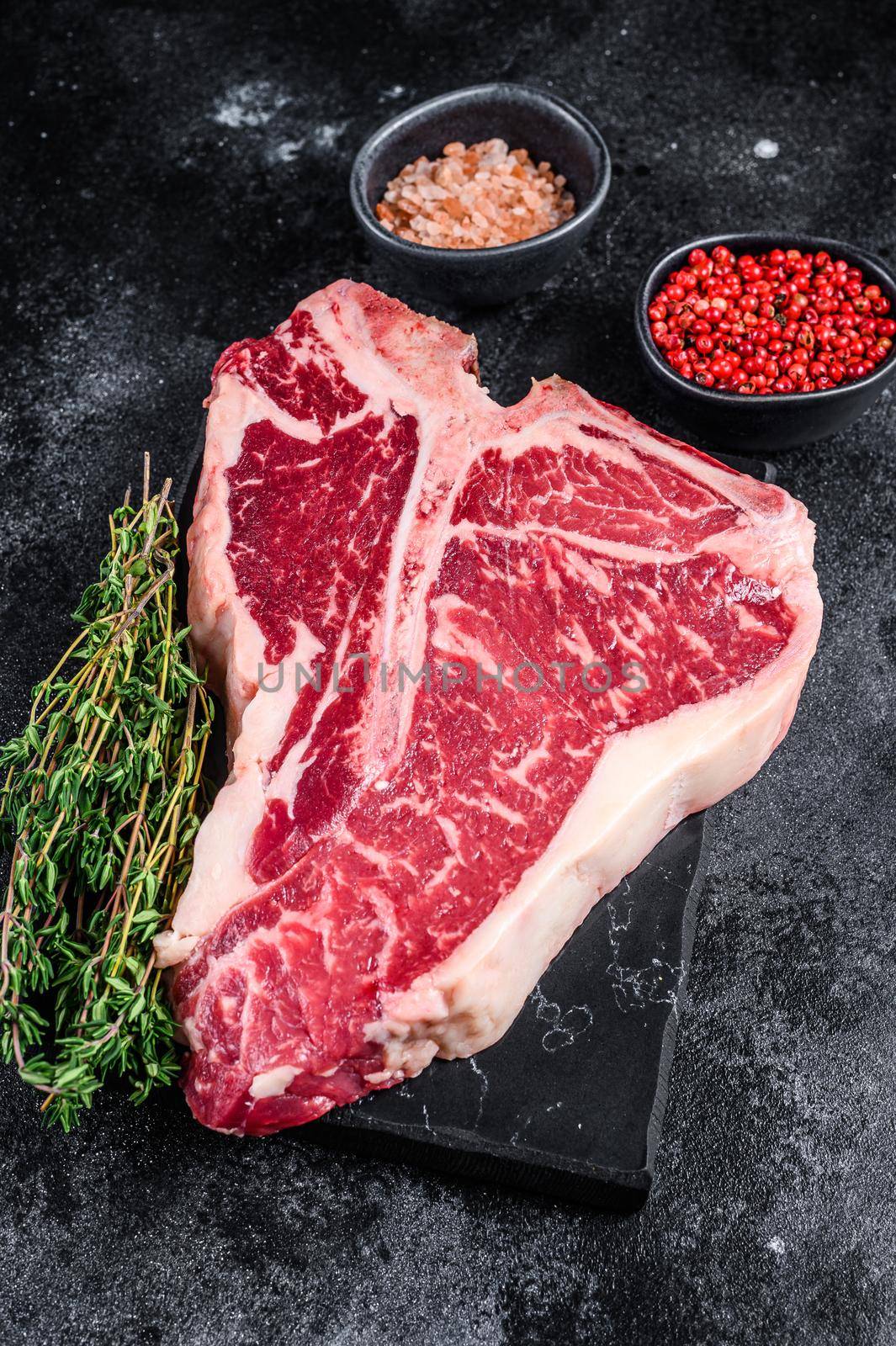 Dry-aged Raw T-bone or porterhouse beef meat Steak with herbs and salt. Black background. Top view by Composter