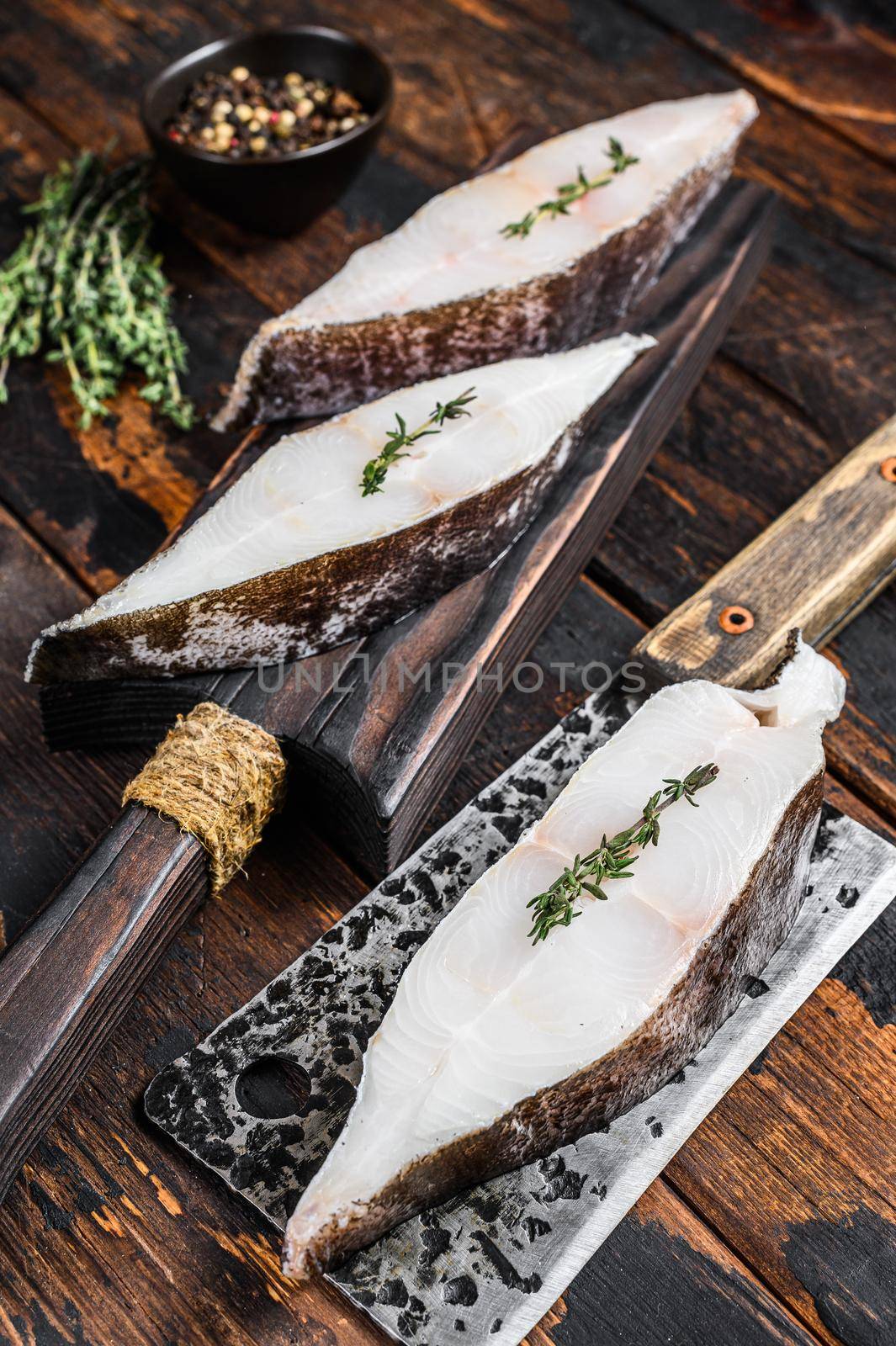 Raw fresh halibut fish steak on a wooden cutiing board. Black background. Top view by Composter