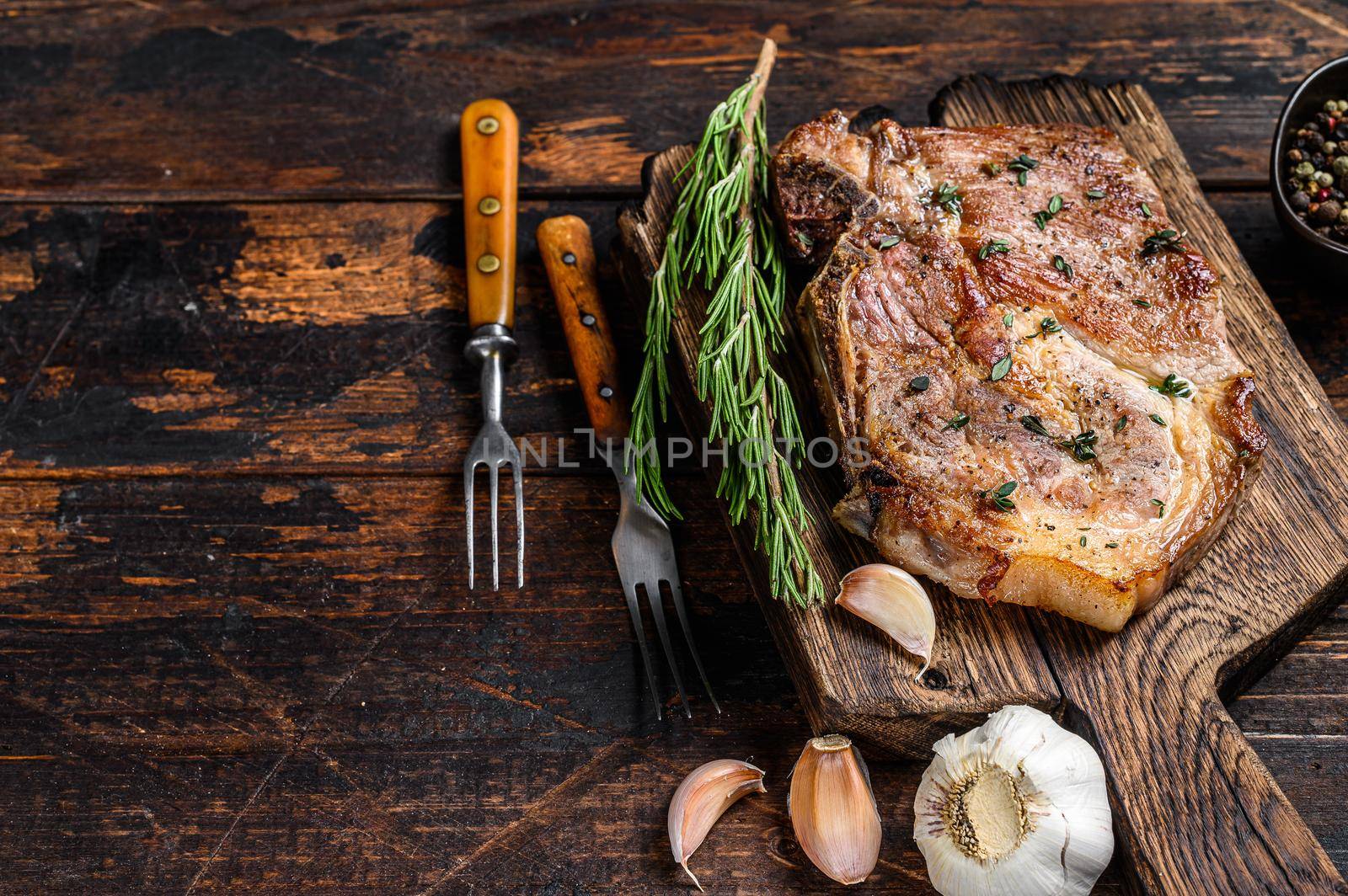 Roasted pork chop steak on a cutting board. Dark wooden background. Top view. Copy space.